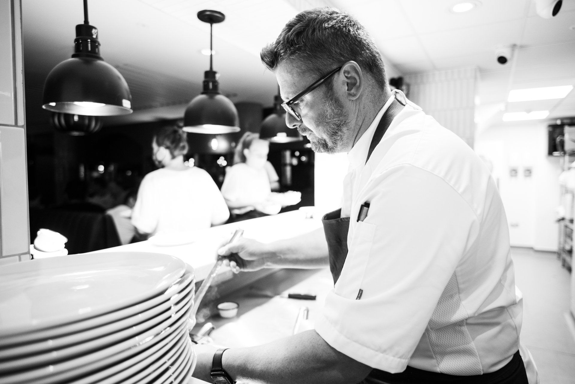 A black and white photo of a chef preparing food in a kitchen.