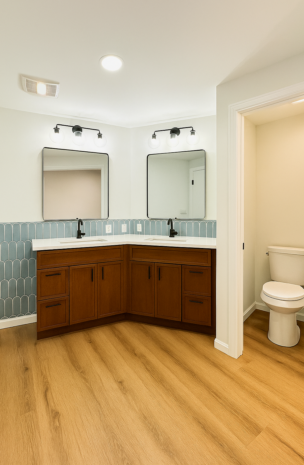 Bathroom with dual sinks, brown cabinets, blue tile backsplash, mirrors, toilet, and light wood flooring.
