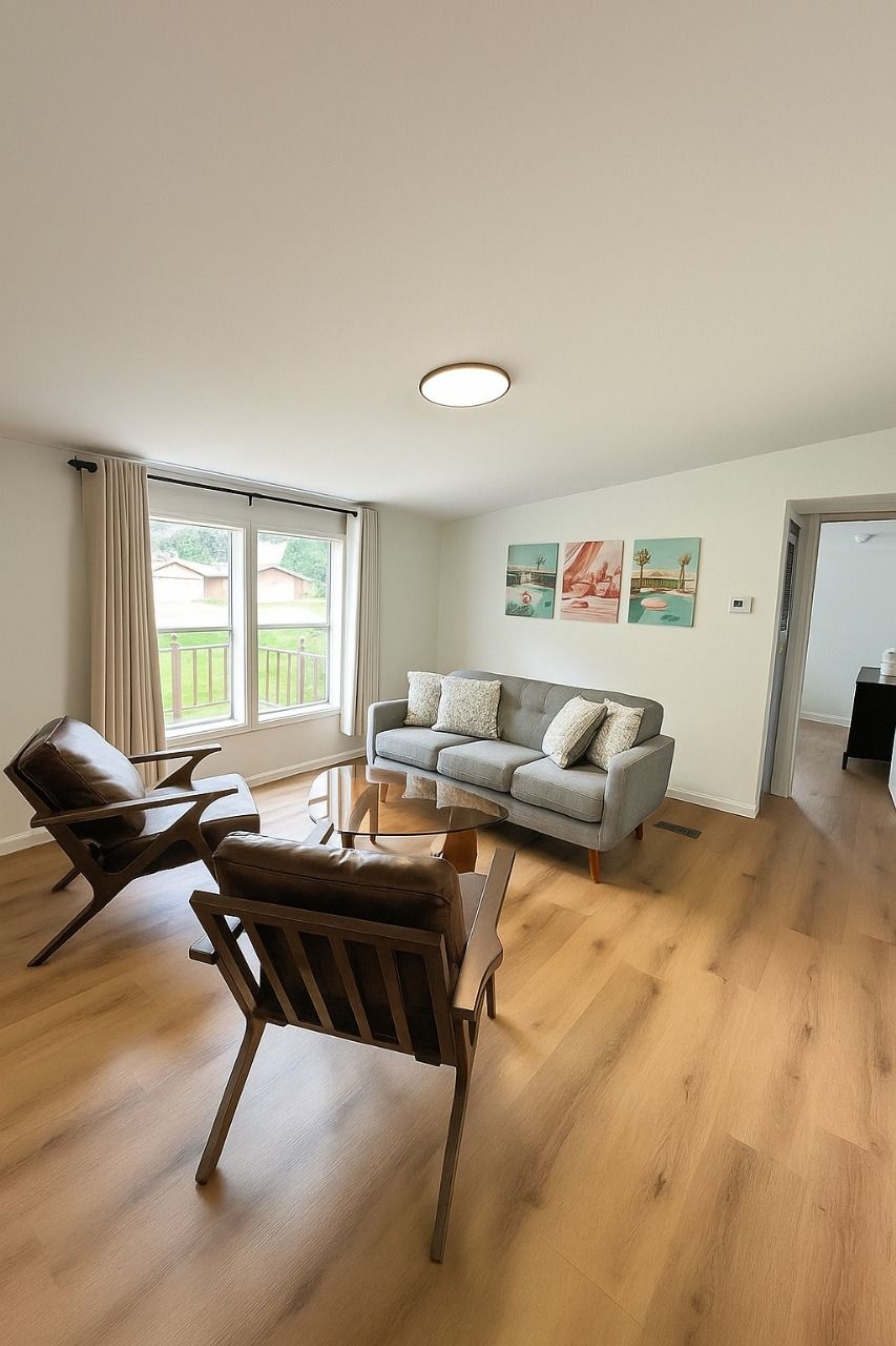 Living room with gray sofa, wooden chairs, and framed artwork; light wood floors.