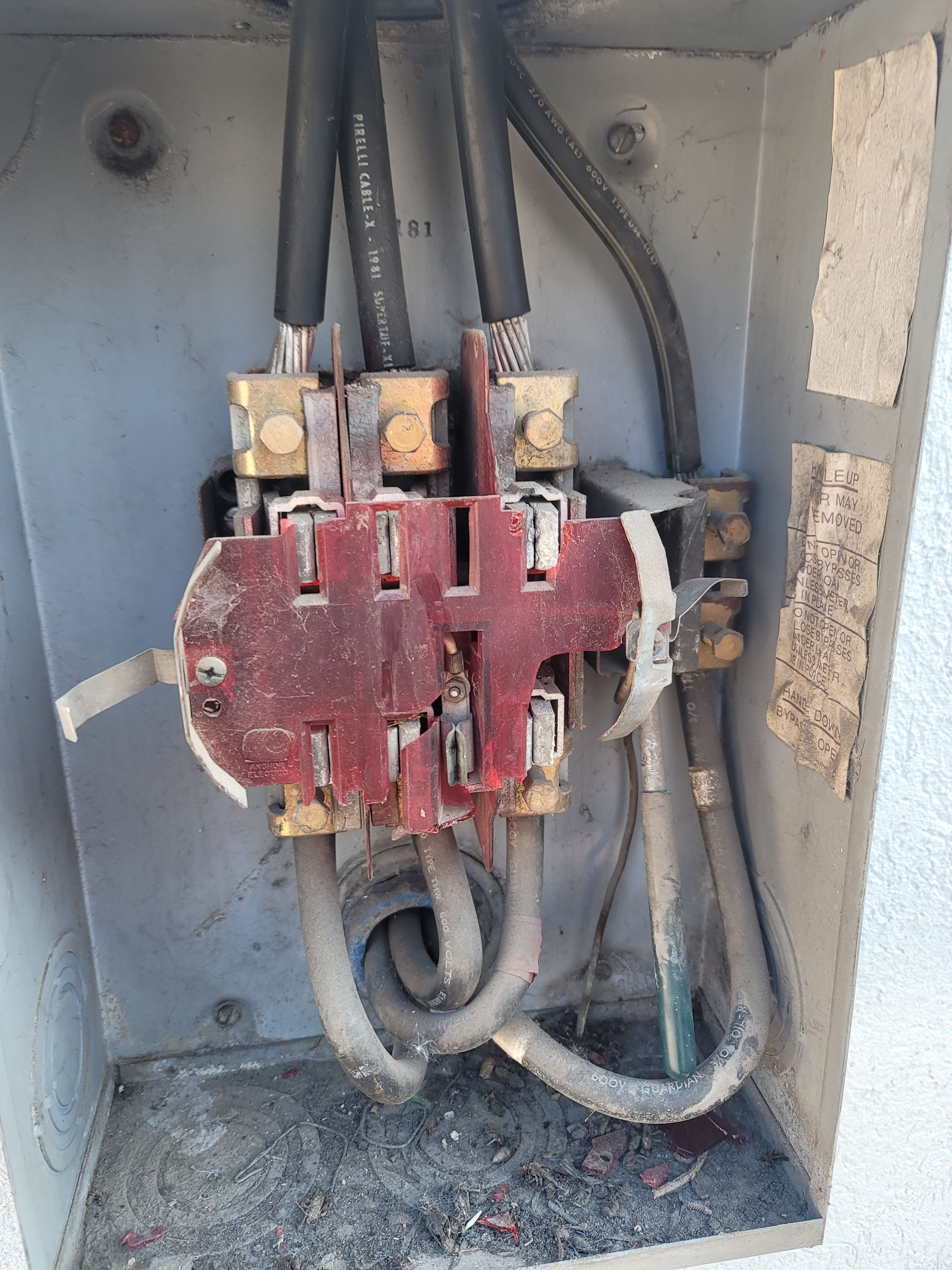 An open electrical meter base box showing damaged red plastic housing and connected wiring inside a metal enclosure.