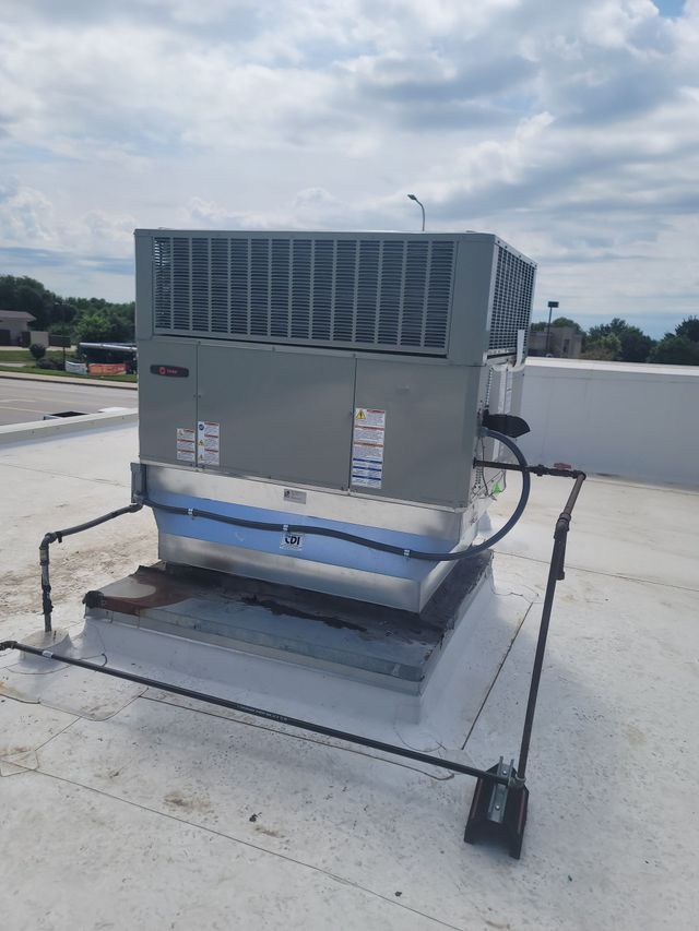 A gray rooftop HVAC unit on a white flat roof, surrounded by a black metal safety railing against a blue sky.