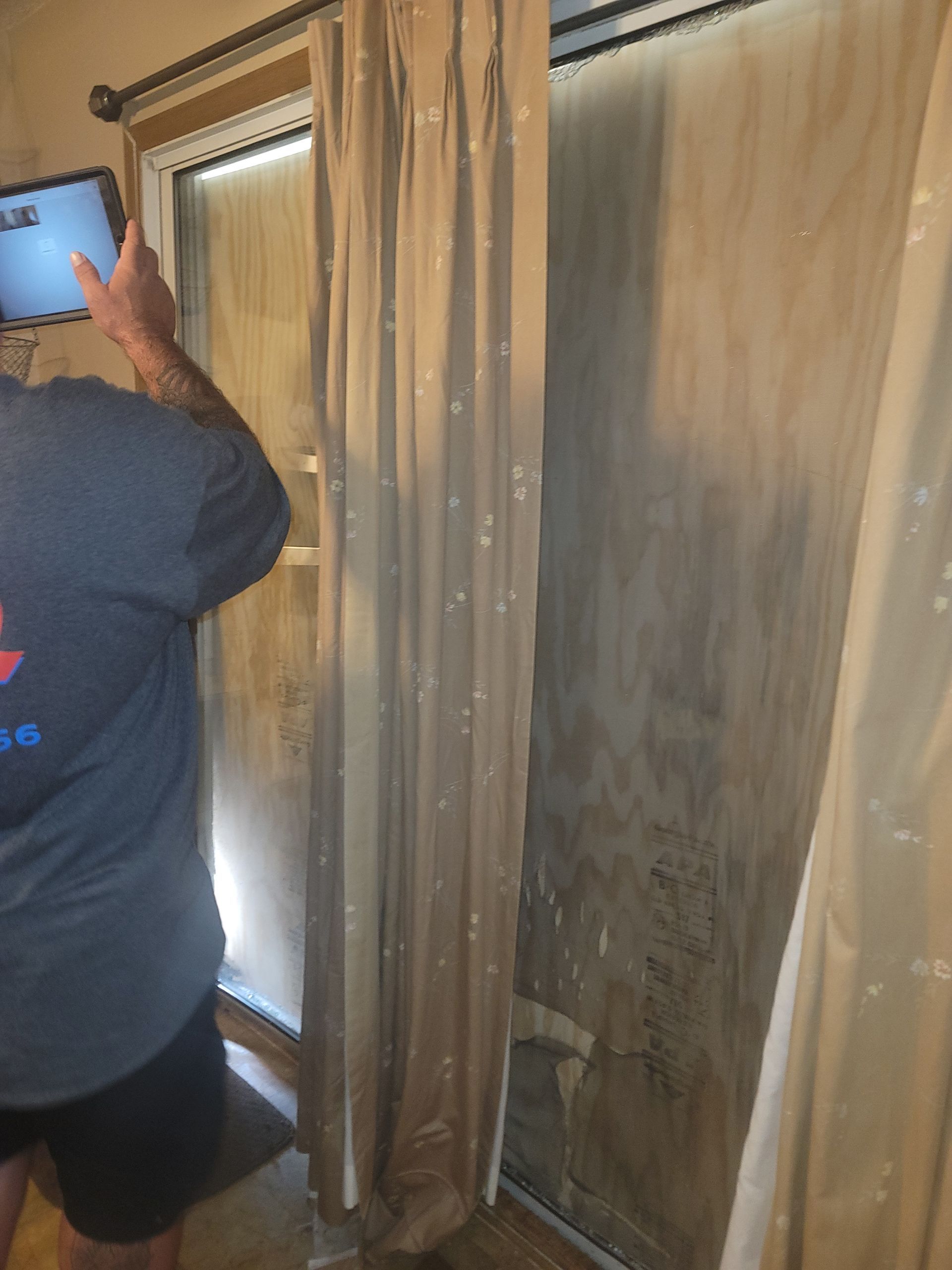 A person in a gray shirt uses a tablet to photograph a wall area showing signs of significant water damage and staining.