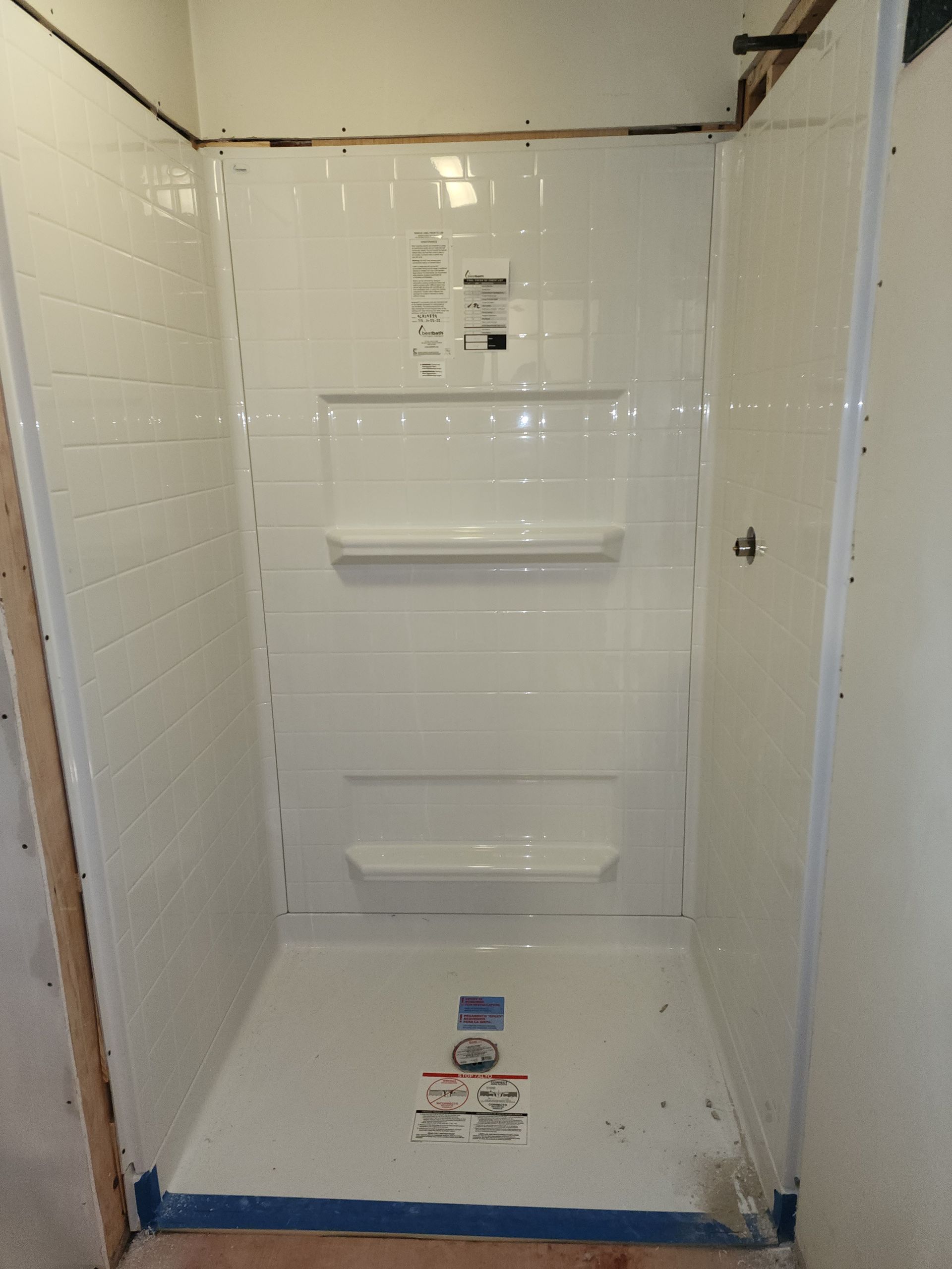 A white, newly installed shower stall with a built-in shelf and soap niche, set within an unfinished bathroom frame.