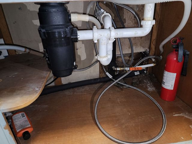 Under-sink plumbing with a black drain trap, coiled hose, and red fire extinguisher on the floor