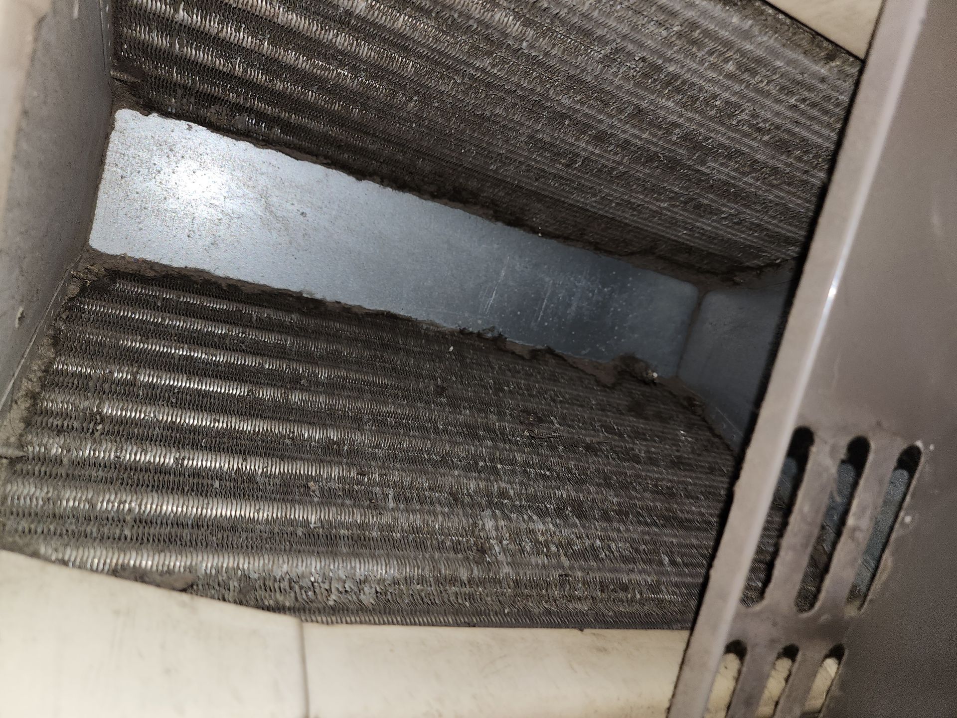 A close-up view of dirty, dust-covered air conditioner cooling coils inside a metal housing.