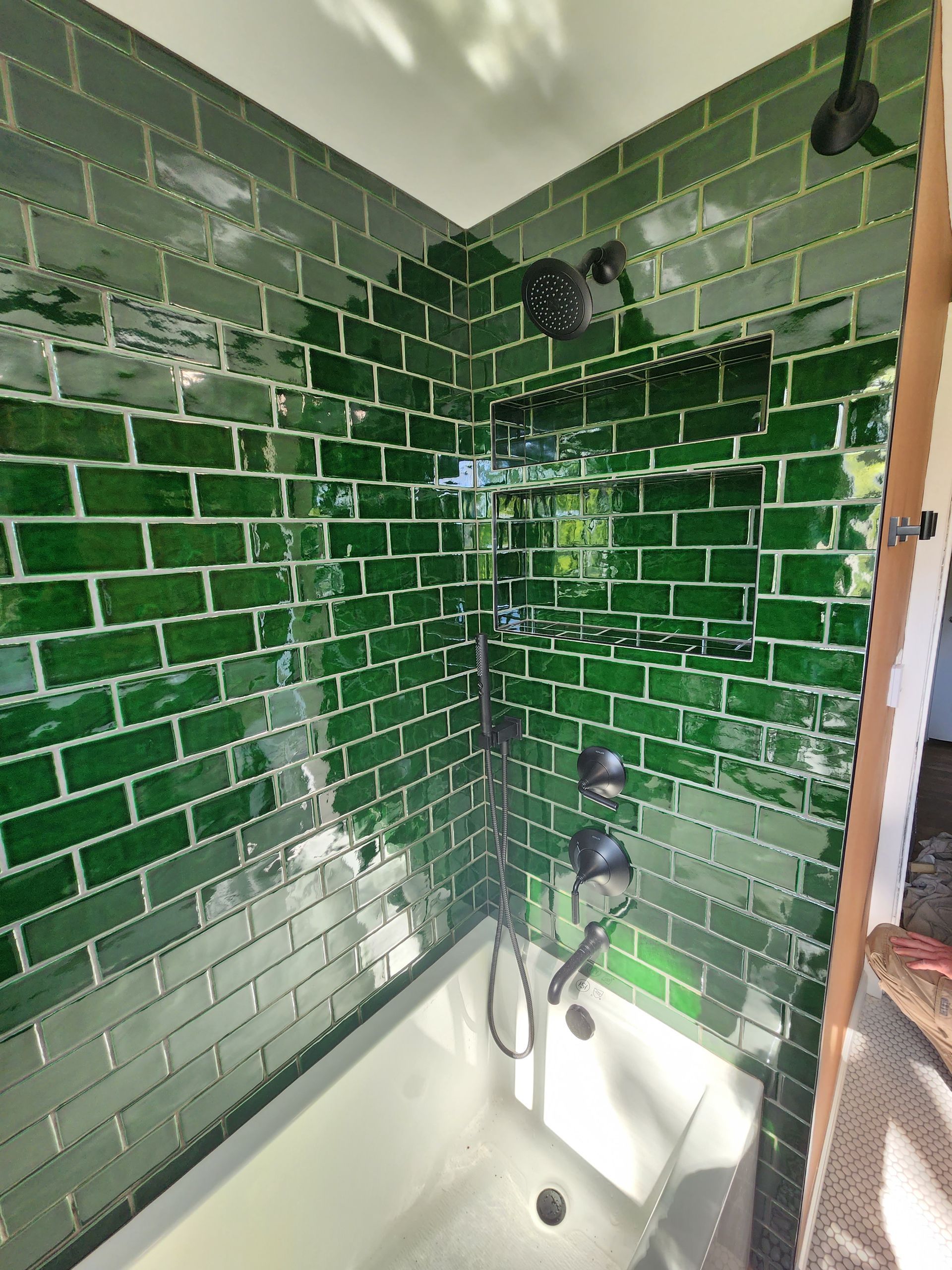 A shower area with glossy emerald green subway tiles, matte black fixtures, and a built-in recessed niche.