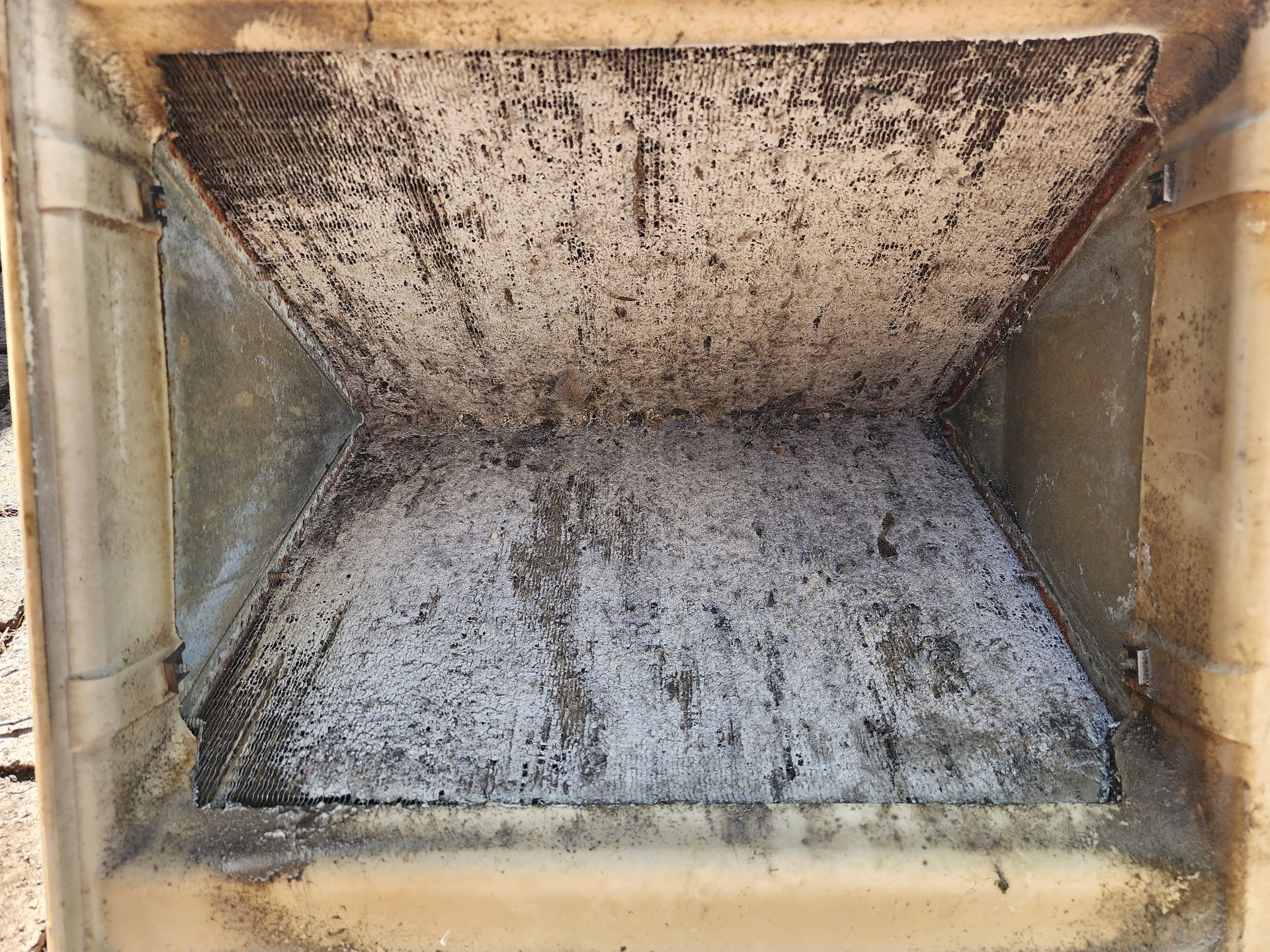 An interior view of a dirty, beige industrial hopper or chute with residue covering its angled metal walls.