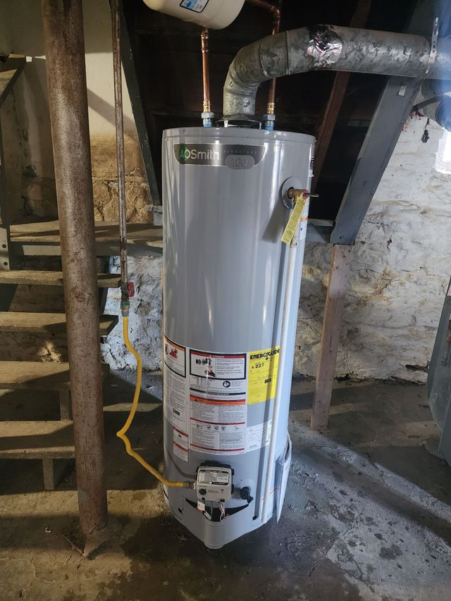White water heater in a basement utility area with pipes and exposed beams.