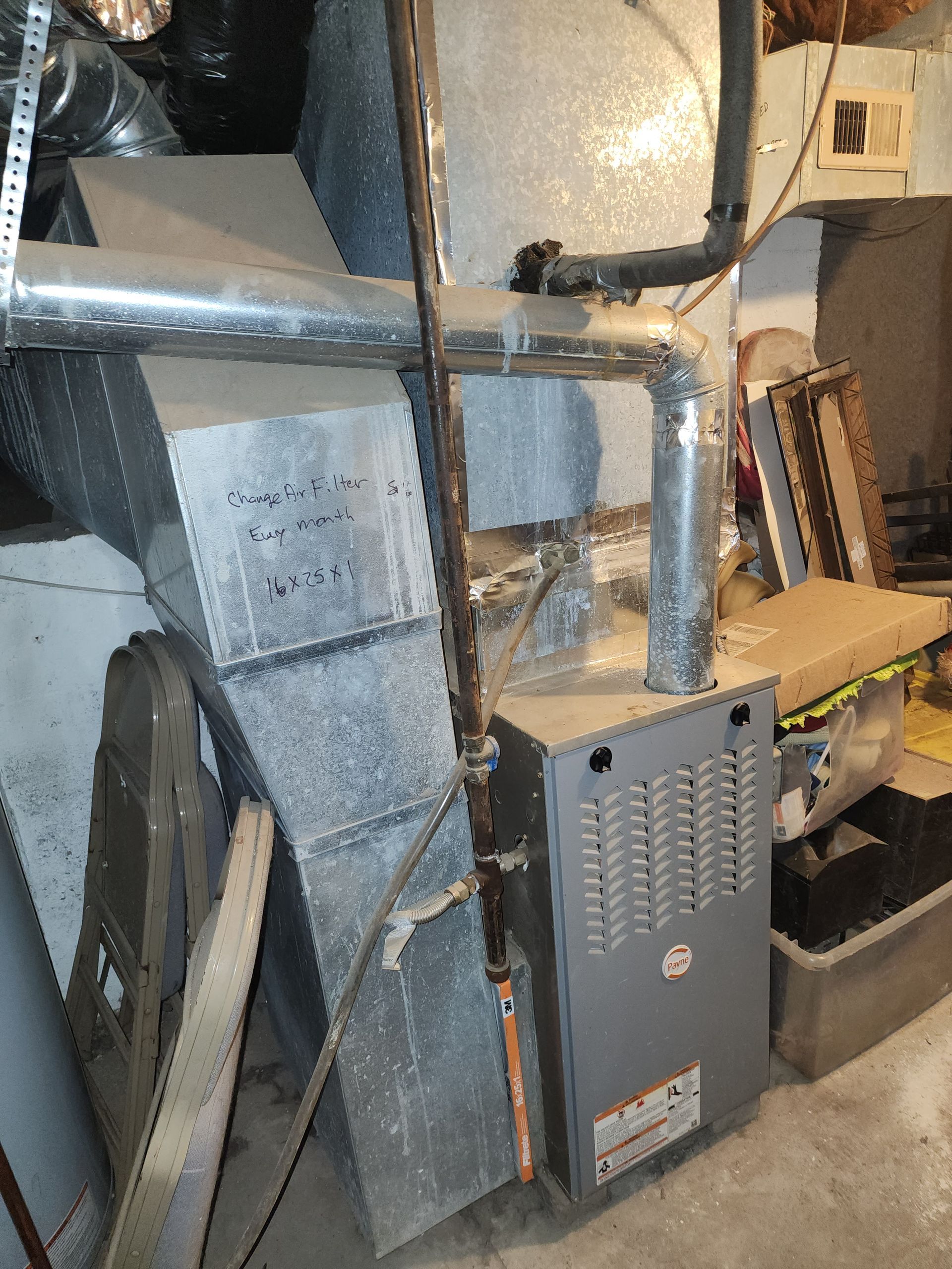 A gray gas furnace with attached metal ductwork installed in a cluttered residential basement.