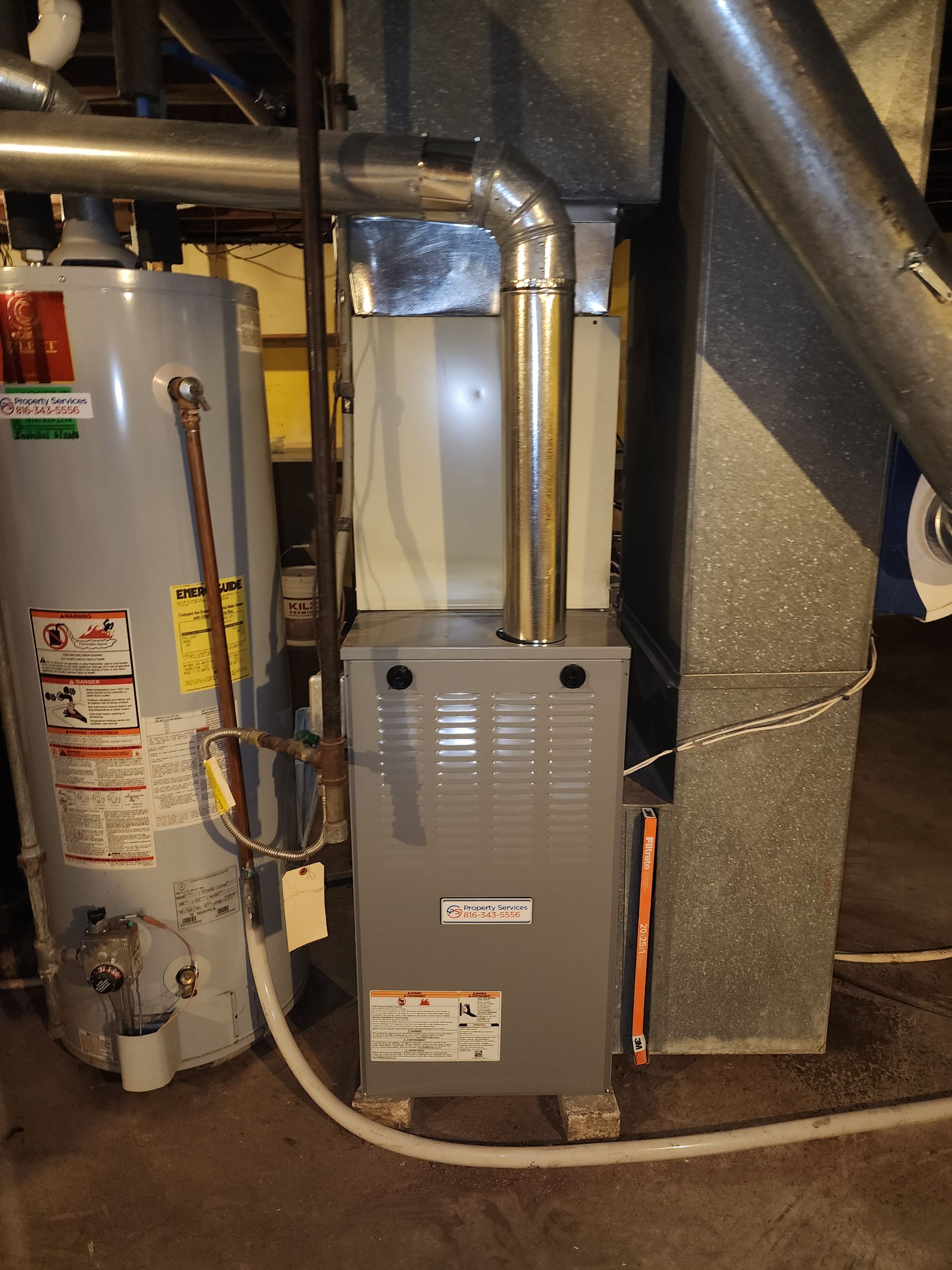 A utility room showing a grey gas furnace next to a tall water heater, with attached metal ventilation ducts.