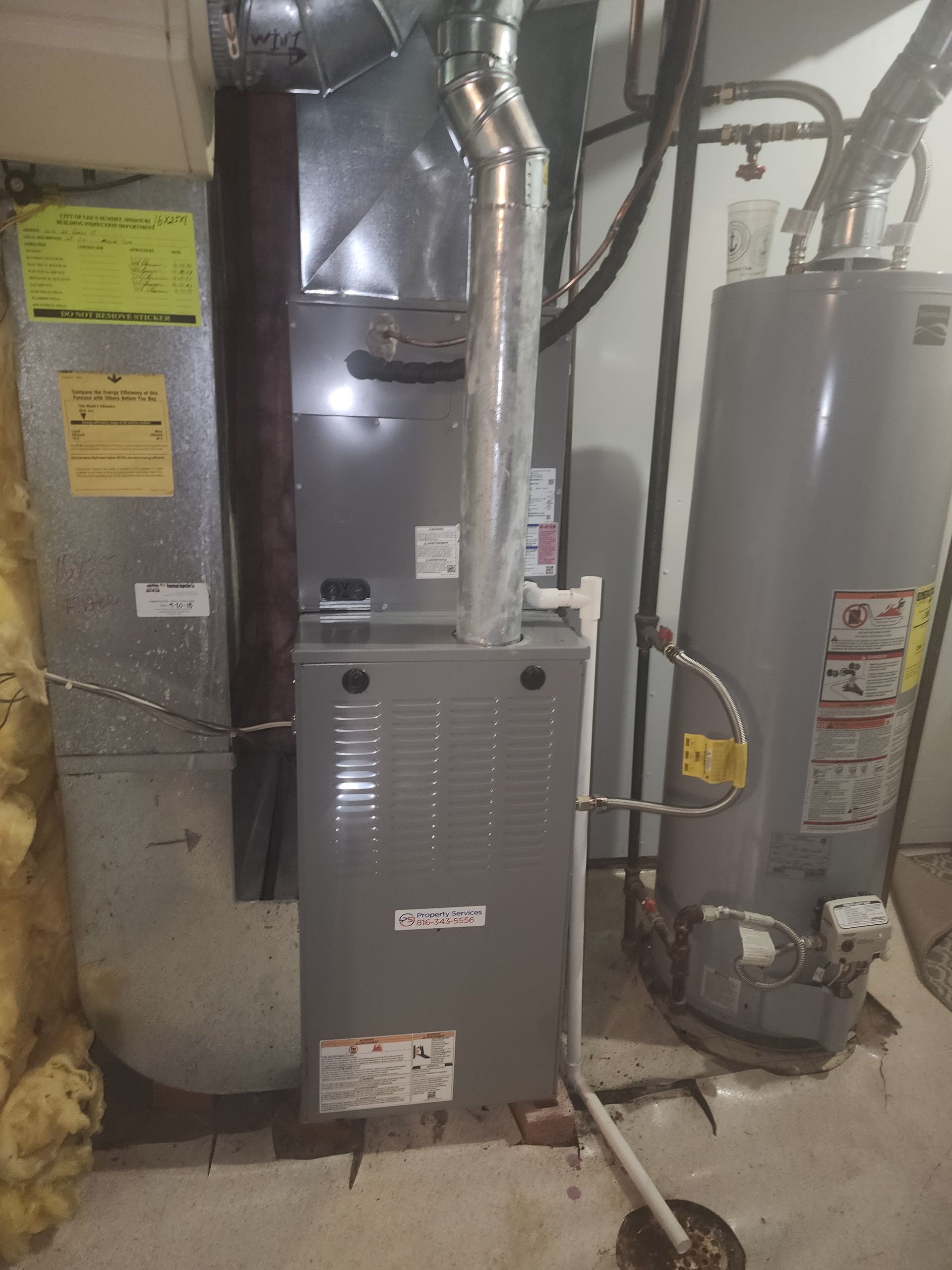 A utility closet featuring a grey gas furnace, a tall water heater, and connecting metal and white PVC piping.