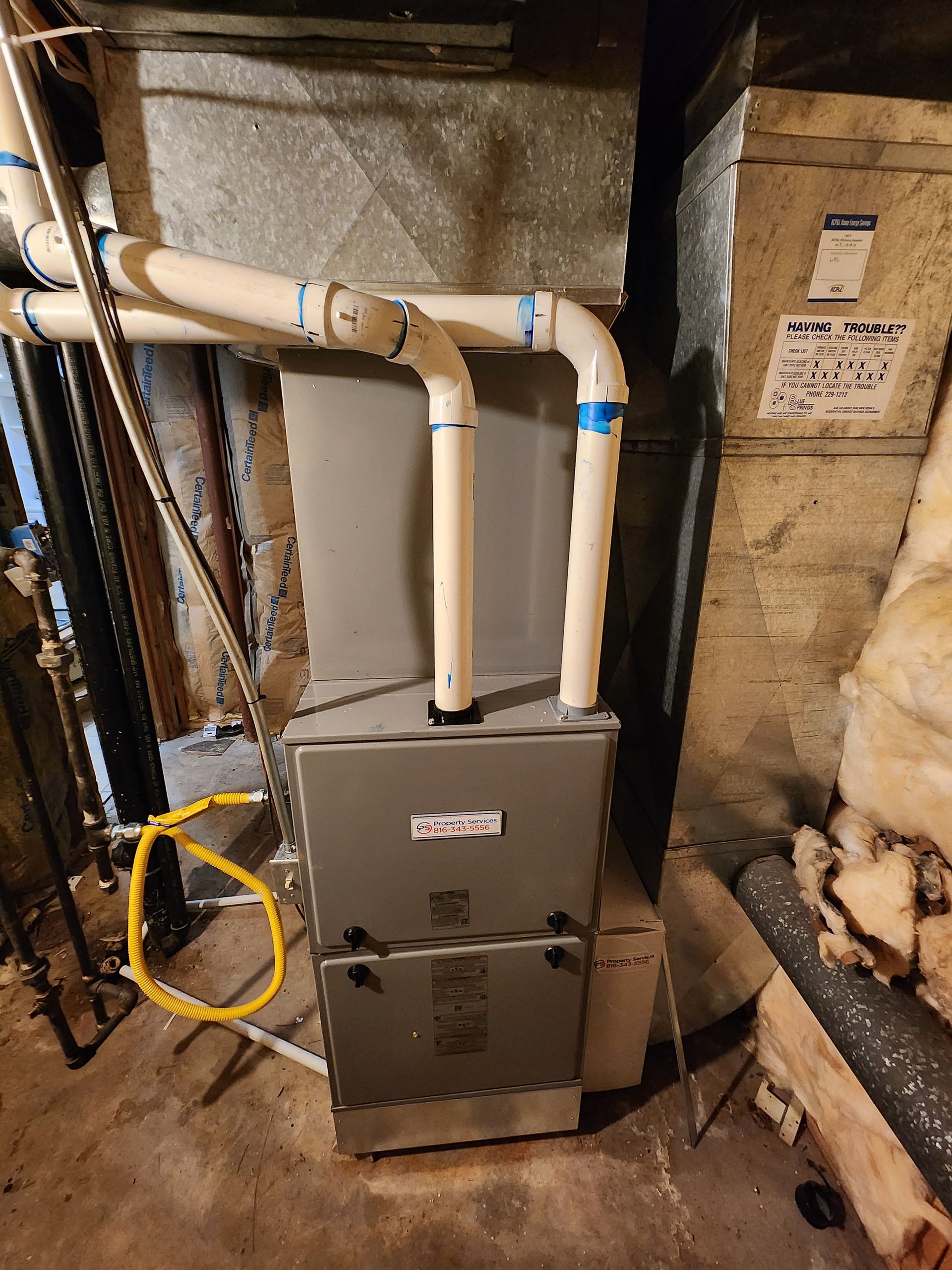 A grey high-efficiency gas furnace in a basement with two white PVC pipes running from its top into the ceiling.