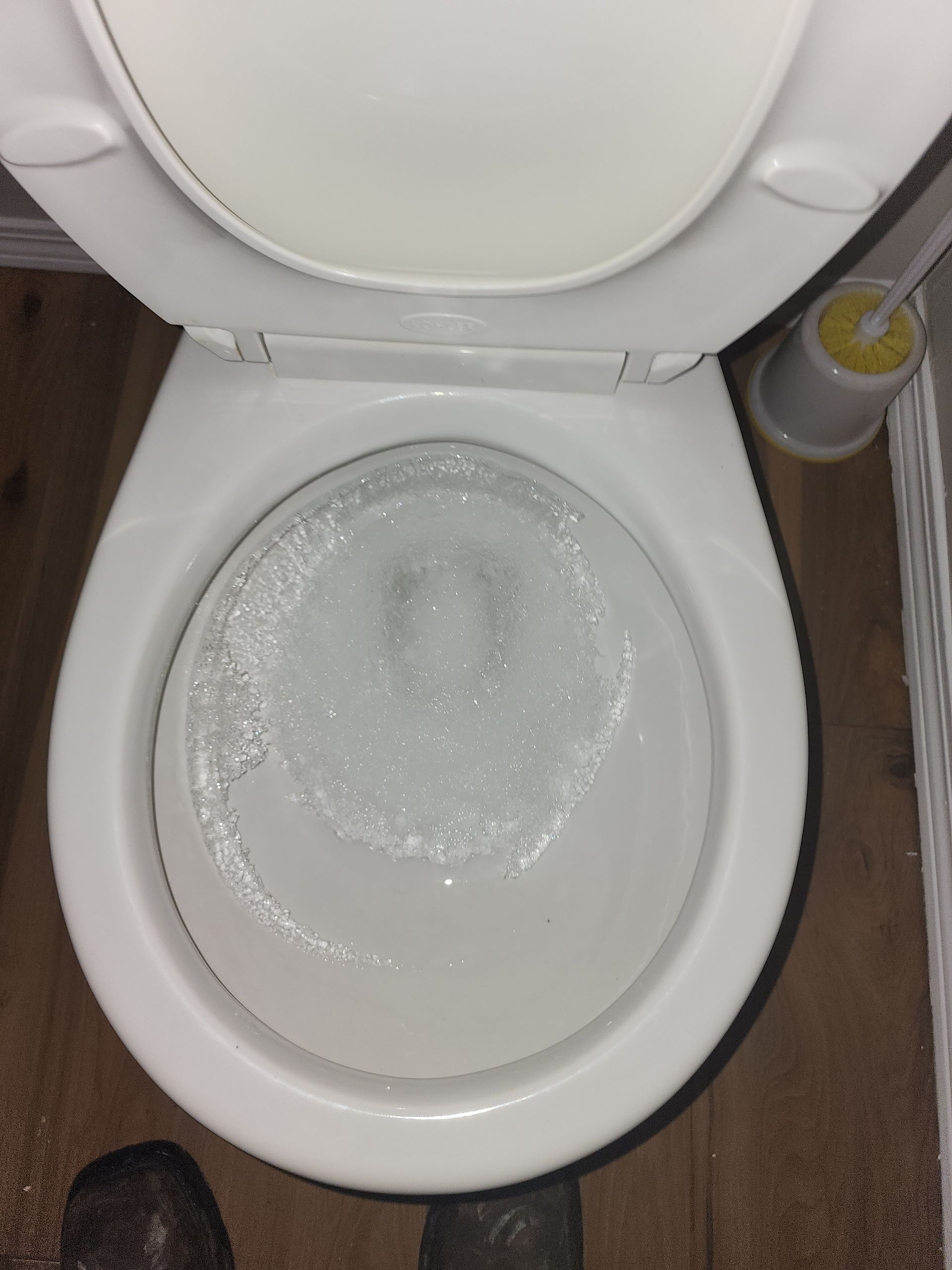A high-angle view looking down into a white porcelain toilet bowl filled with clear, swirling water.