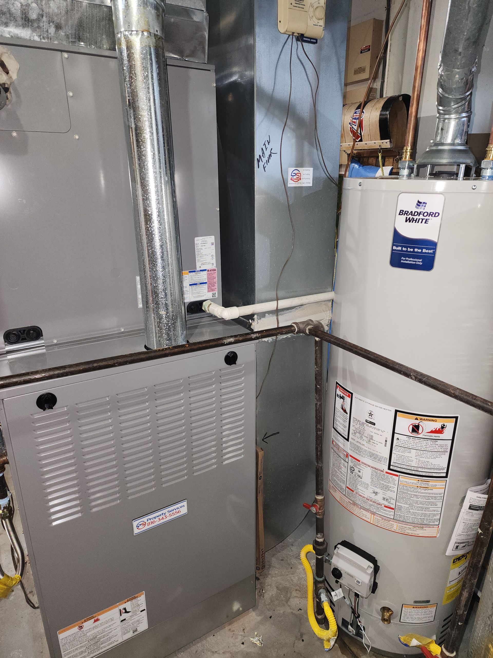 A gray gas furnace and a tall, cylindrical white water heater situated in a residential utility room.