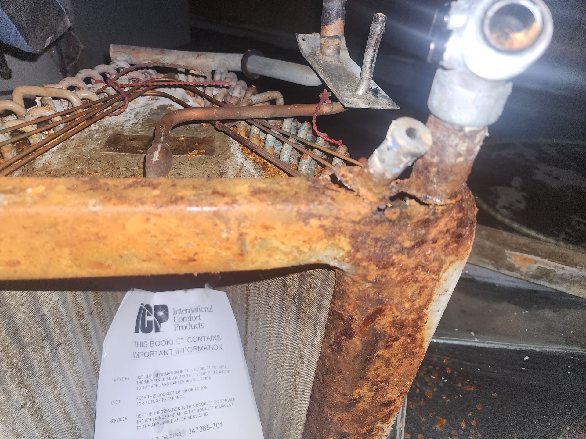 A heavily rusted metal HVAC evaporator coil unit with visible copper tubing and a manufacturer label.