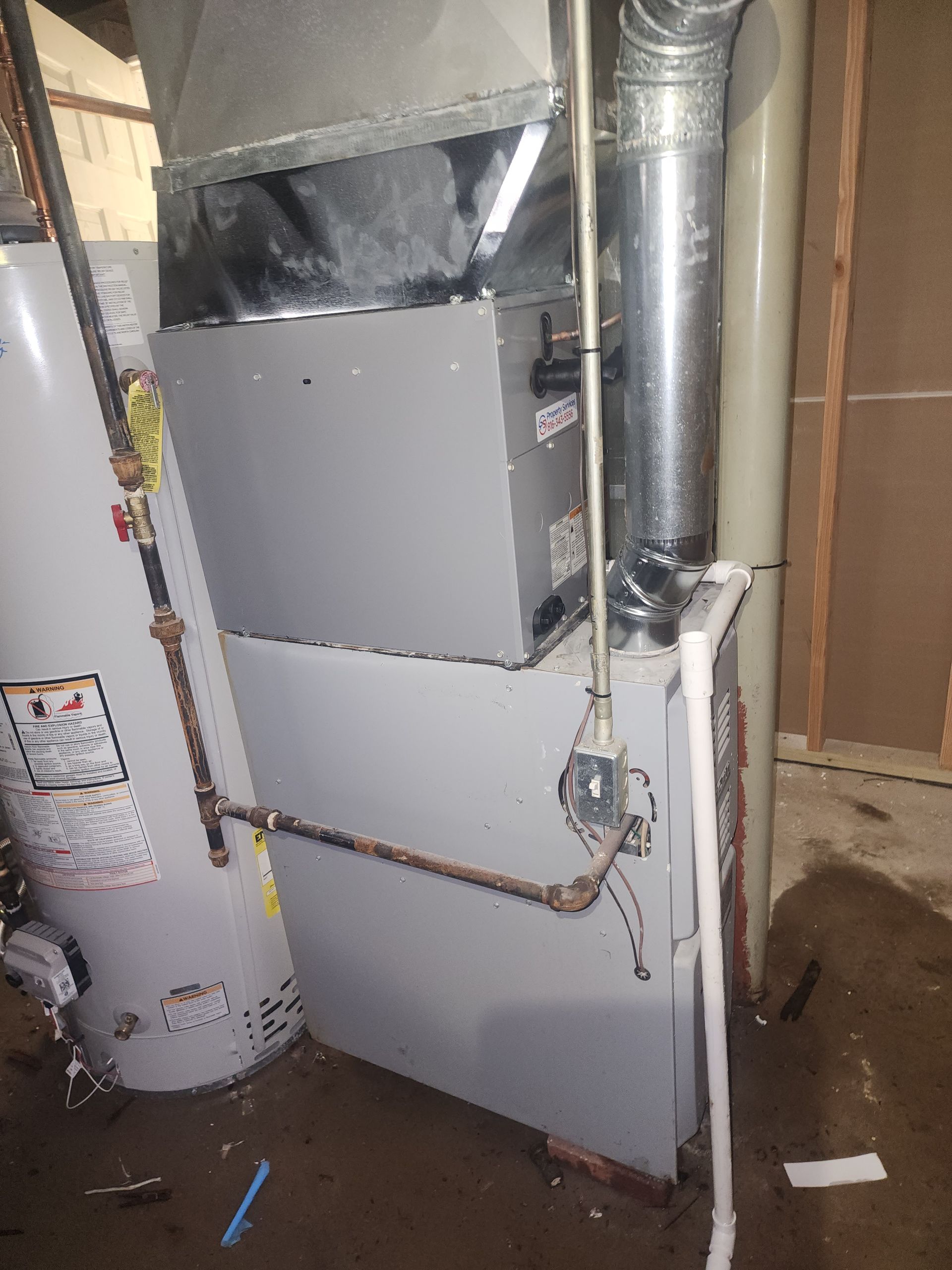 A gray furnace and water heater sit in a utility room, connected by metal ductwork and piping.