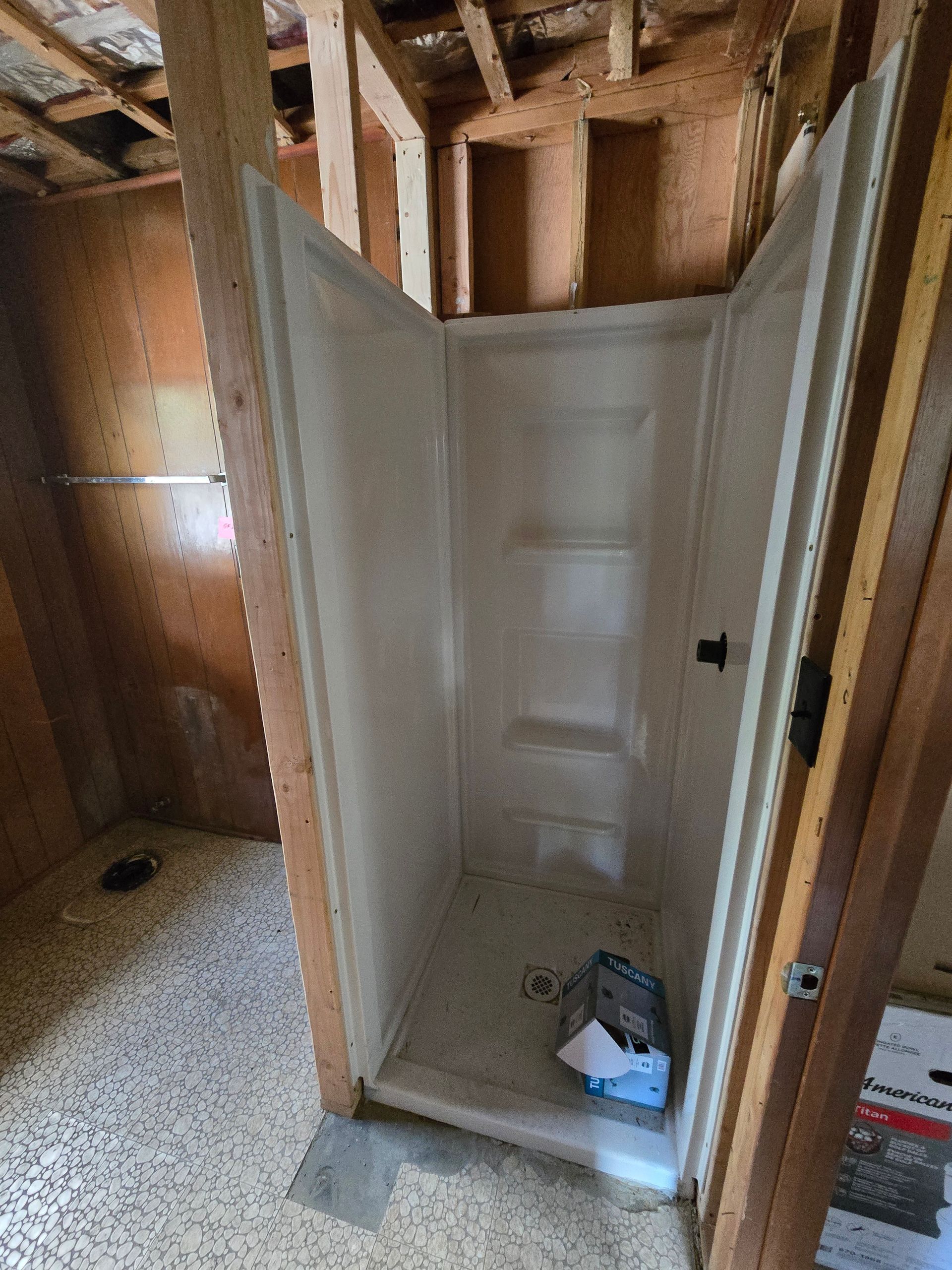 A white shower stall unit installed in a bathroom under construction with exposed wooden wall studs.