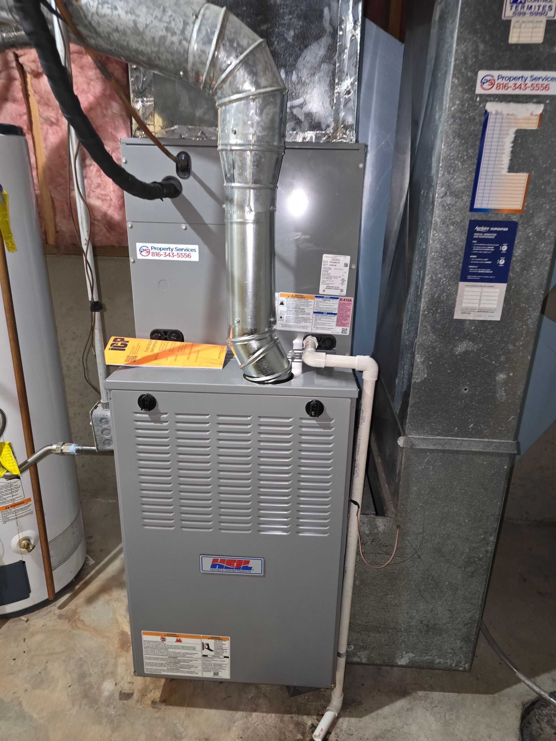 A grey furnace with a metal vent pipe and PVC condensation lines in a residential utility space.