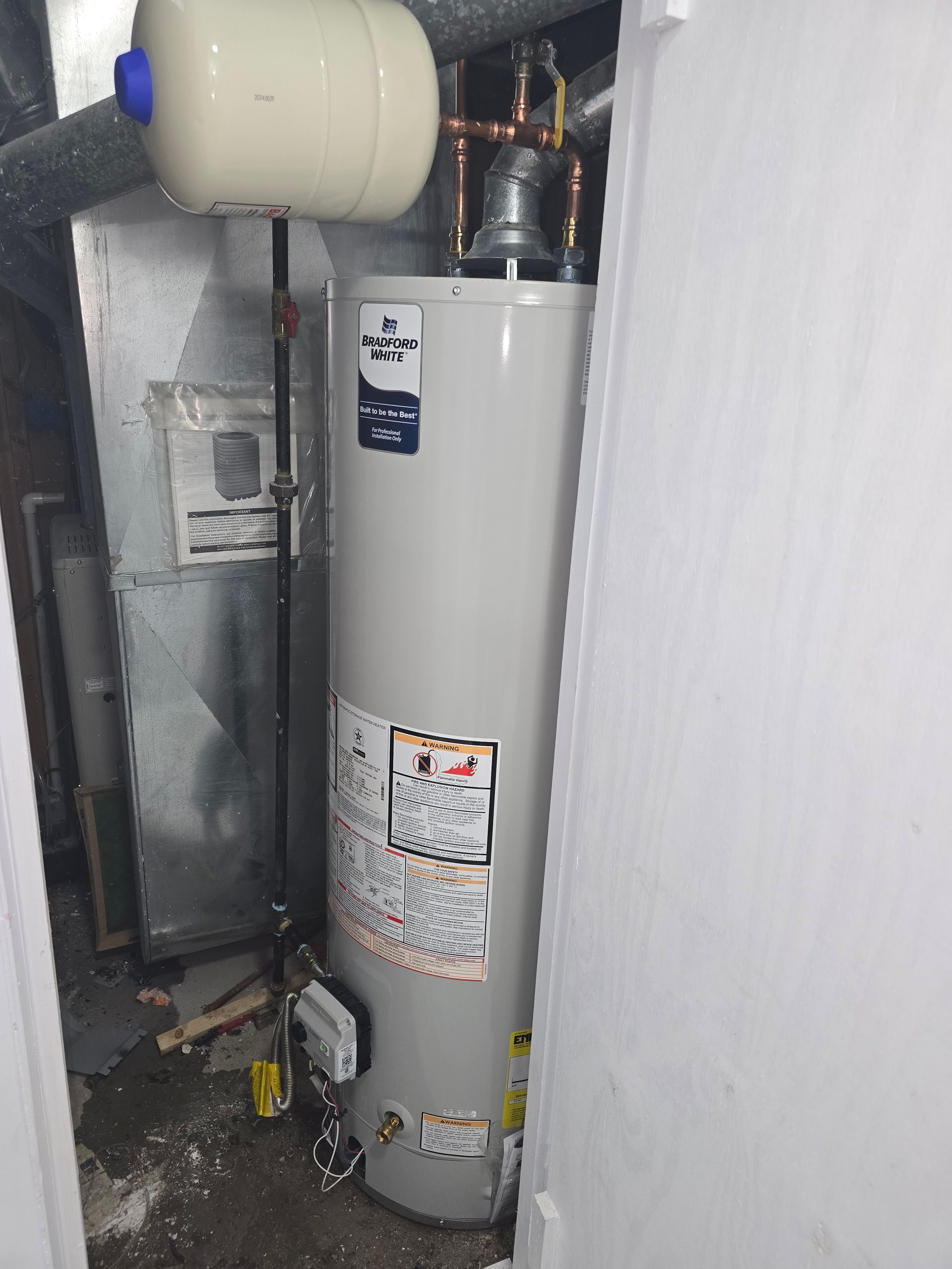 A gray residential water heater and expansion tank installed in a utility closet with copper piping.