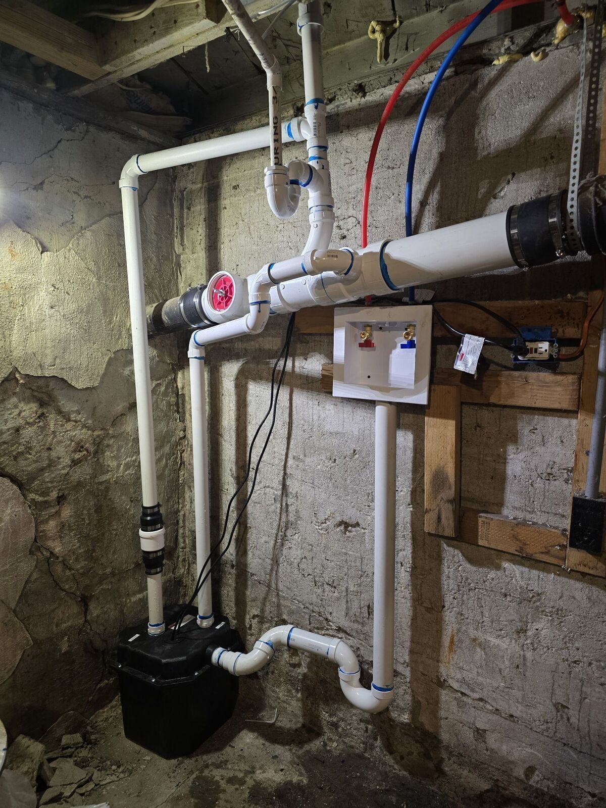 Laundry sink pump system installed against a concrete basement wall with white PVC plumbing and water supply valves.