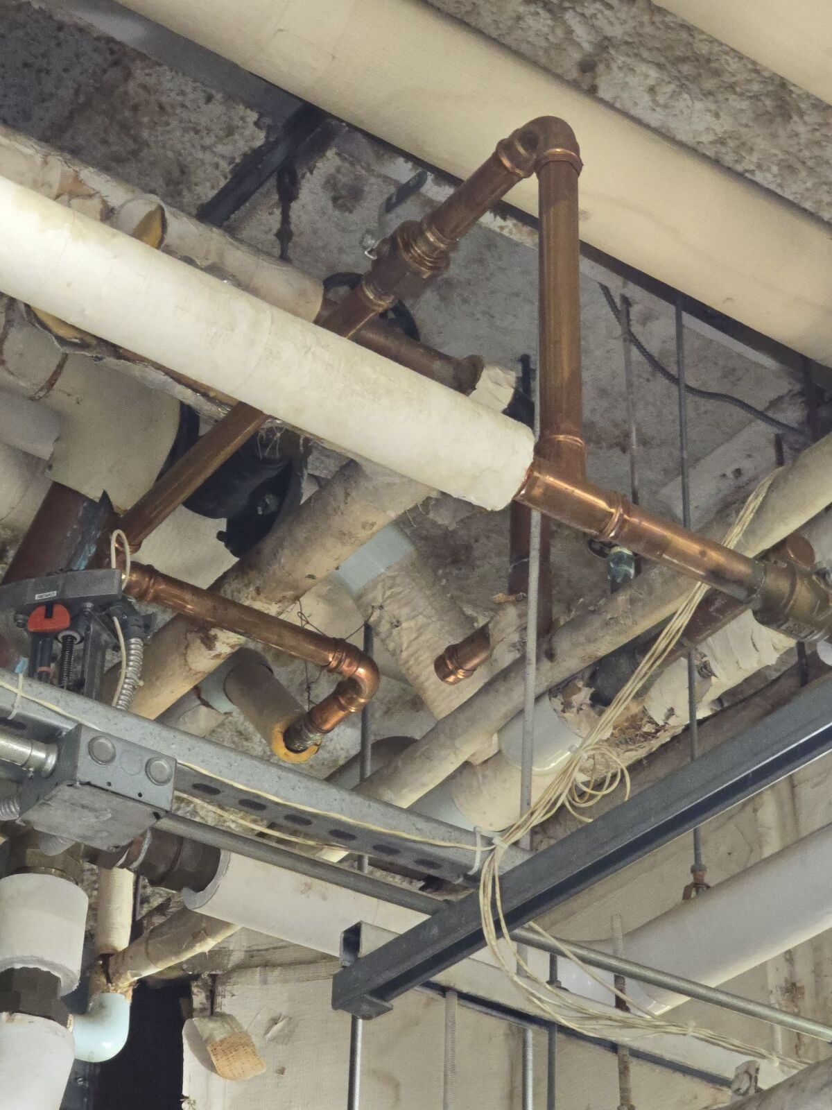 A network of copper and white insulated pipes mounted to a grey concrete ceiling.