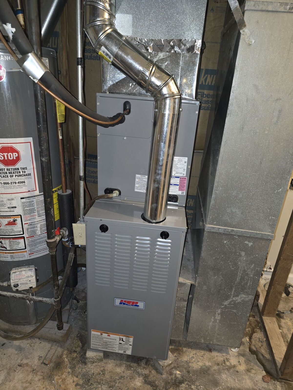 A gray furnace with a metal exhaust pipe positioned next to a water heater in a basement setting.