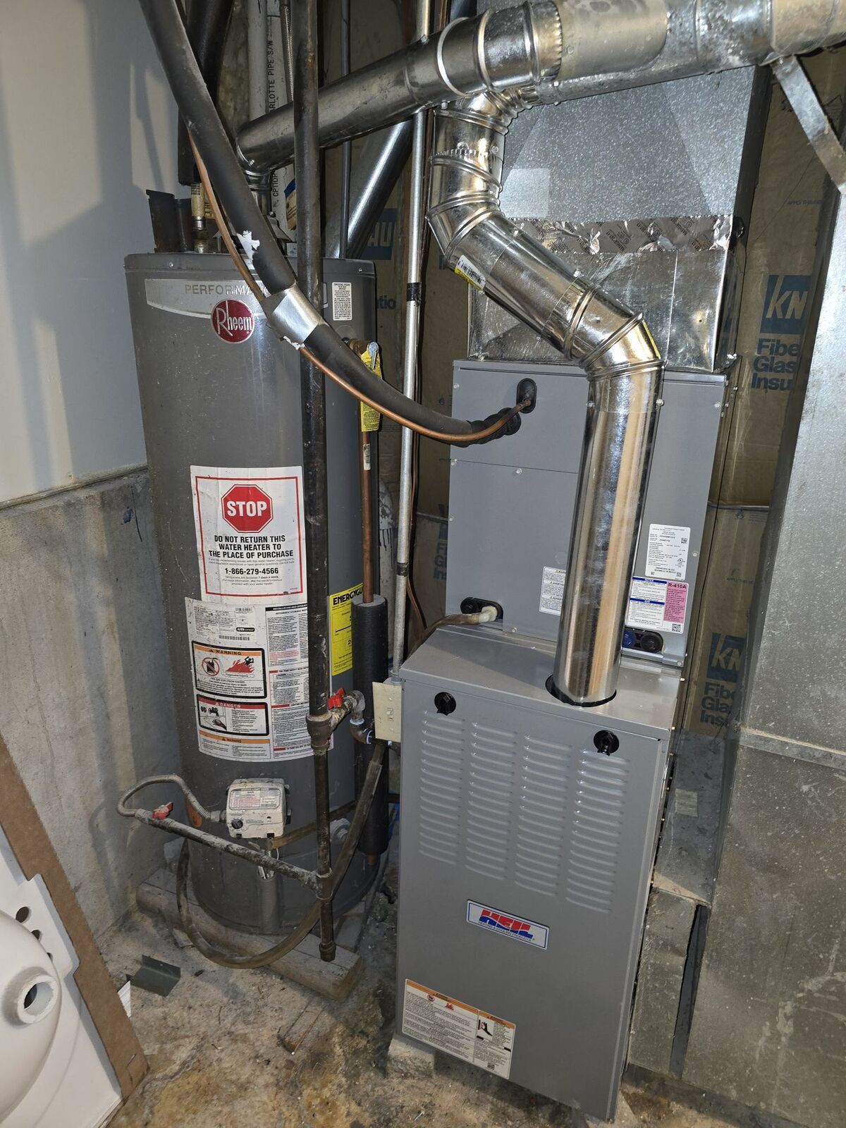 A gray water heater and a gas furnace installed side-by-side in a basement setting with metal vent pipes.