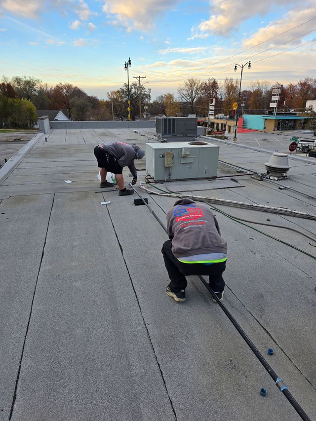 Workers repairing a flat roof at sunset, kneeling near HVAC units and scattered tools.