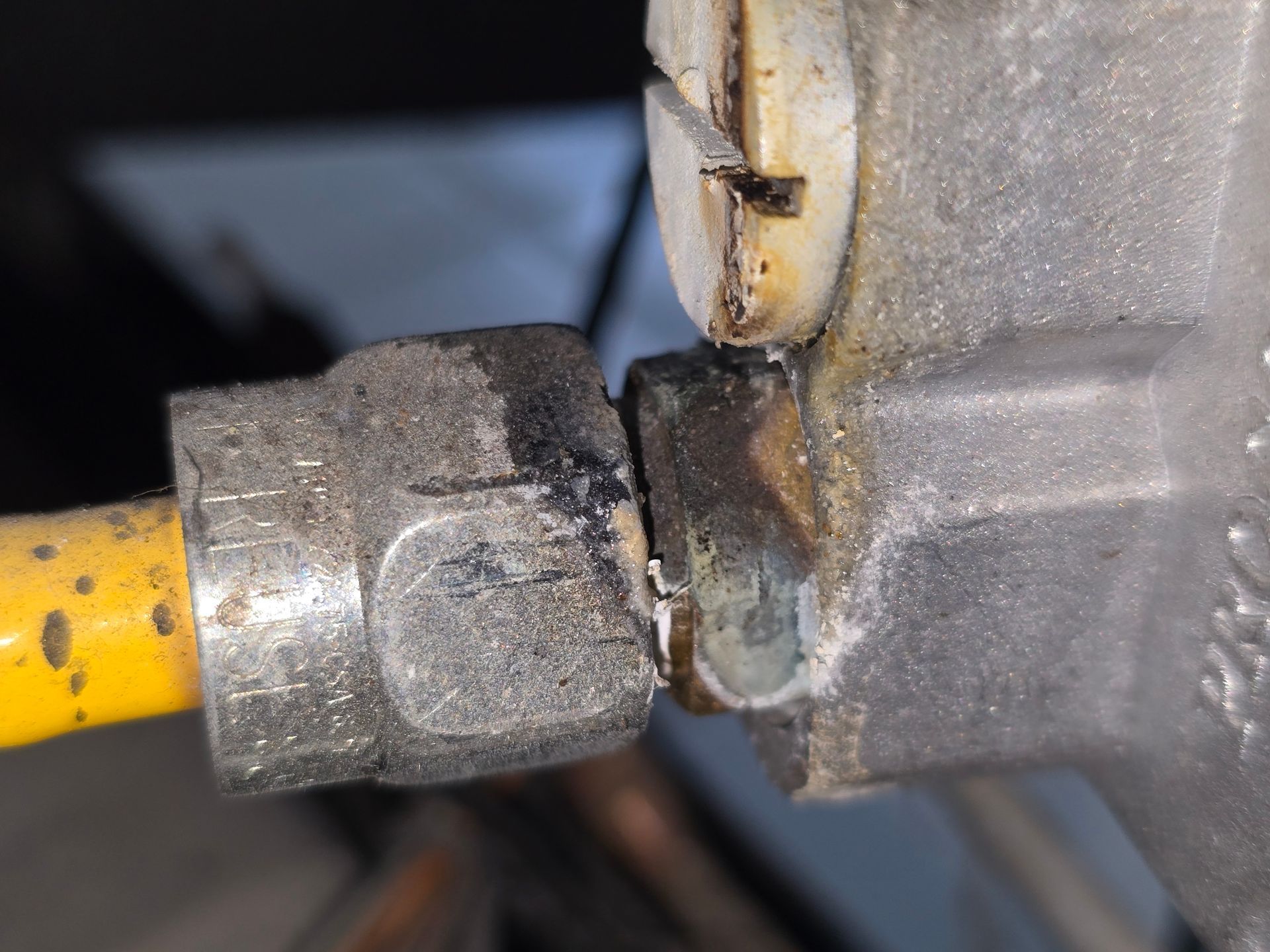 A close-up of a metal pipe fitting connected to a valve, showing signs of corrosion and dark residue at the junction.