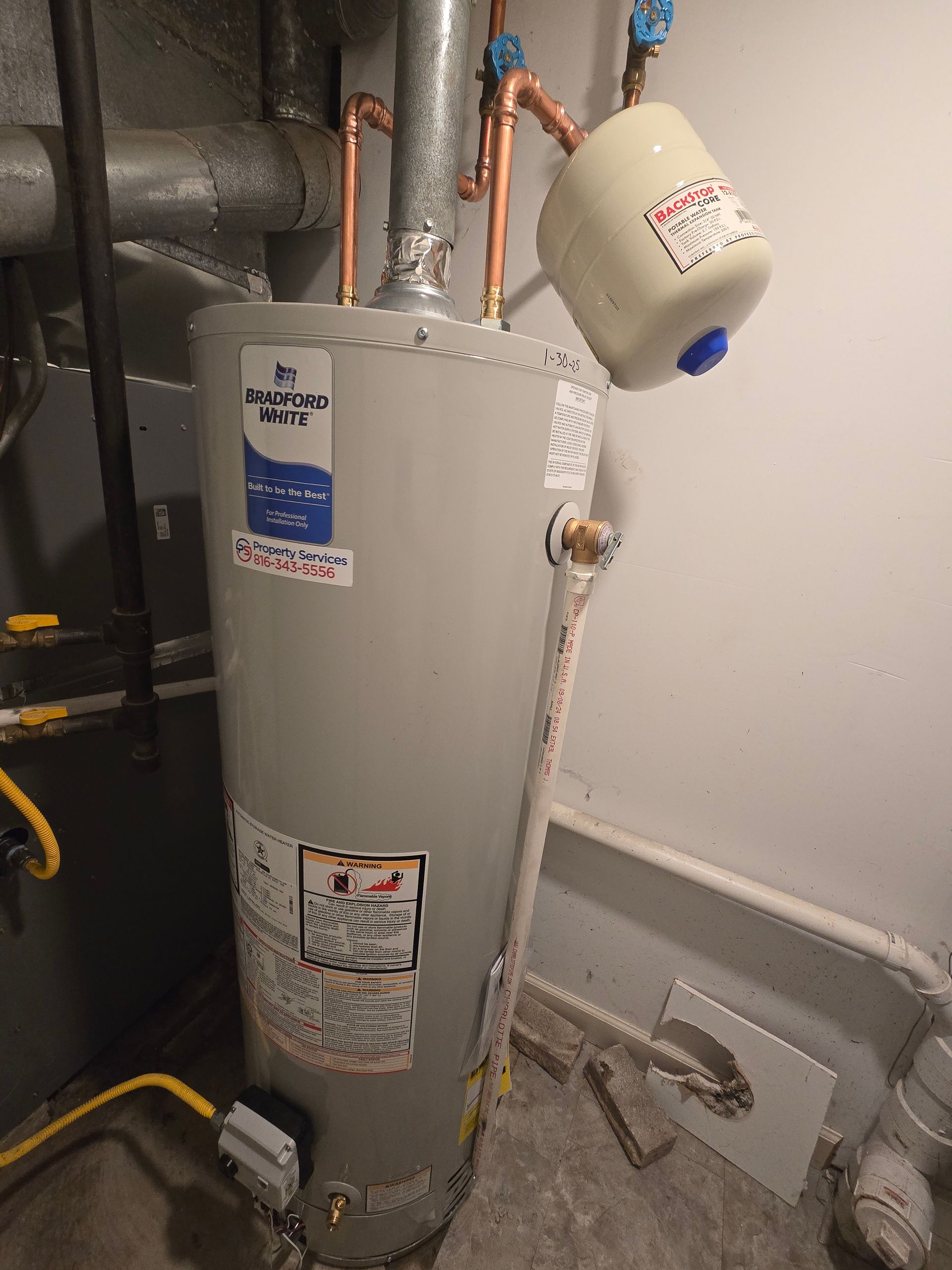 A grey residential water heater with an attached white expansion tank in a basement setting.