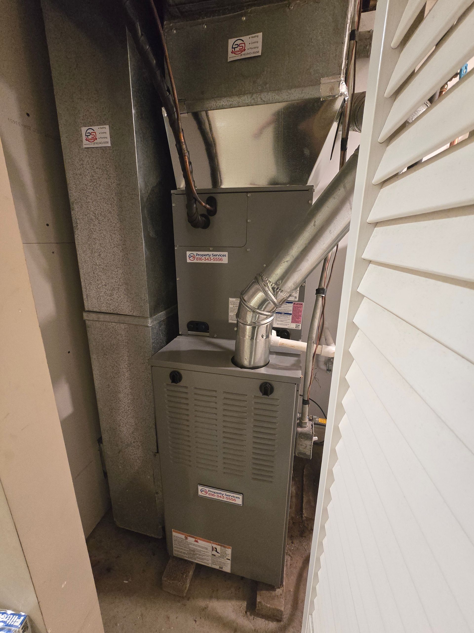 A gray HVAC furnace unit with metal ductwork stands in a narrow utility closet.
