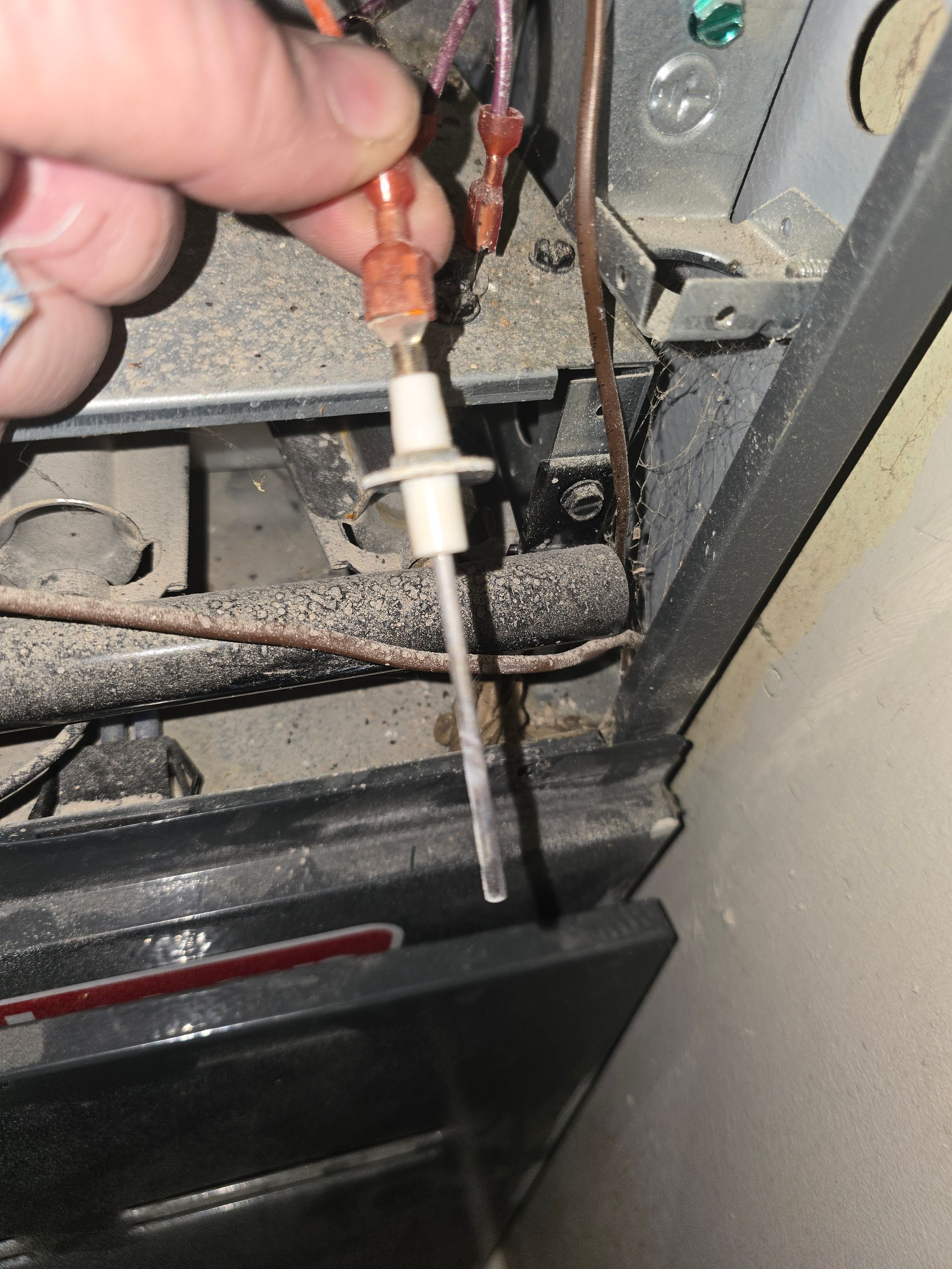 A hand holding a flame sensor from a furnace, showing the metal rod and white ceramic insulator for maintenance.