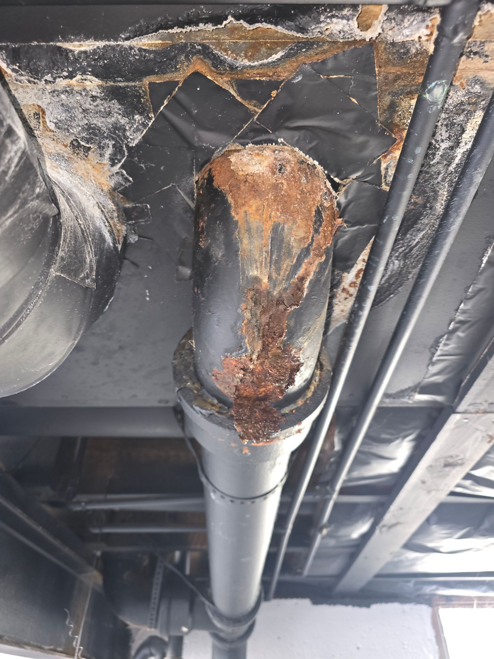 A corroded and rusted pipe elbow joint attached to a ceiling, showing signs of moisture and degradation.