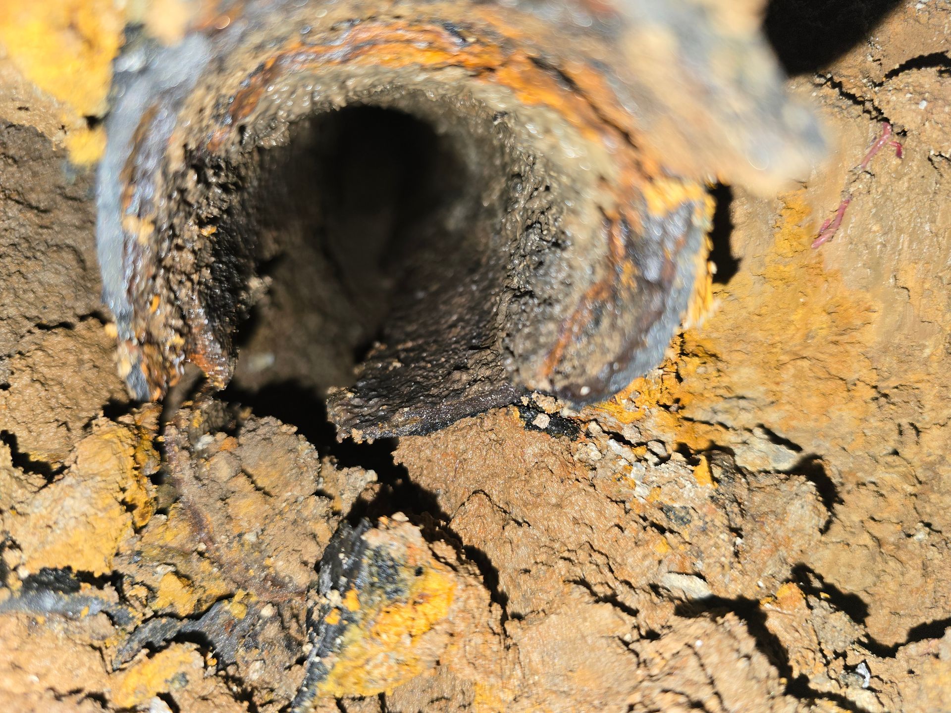 A close-up view looking into a rusted, corroded metal pipe embedded in dry, cracked dirt.