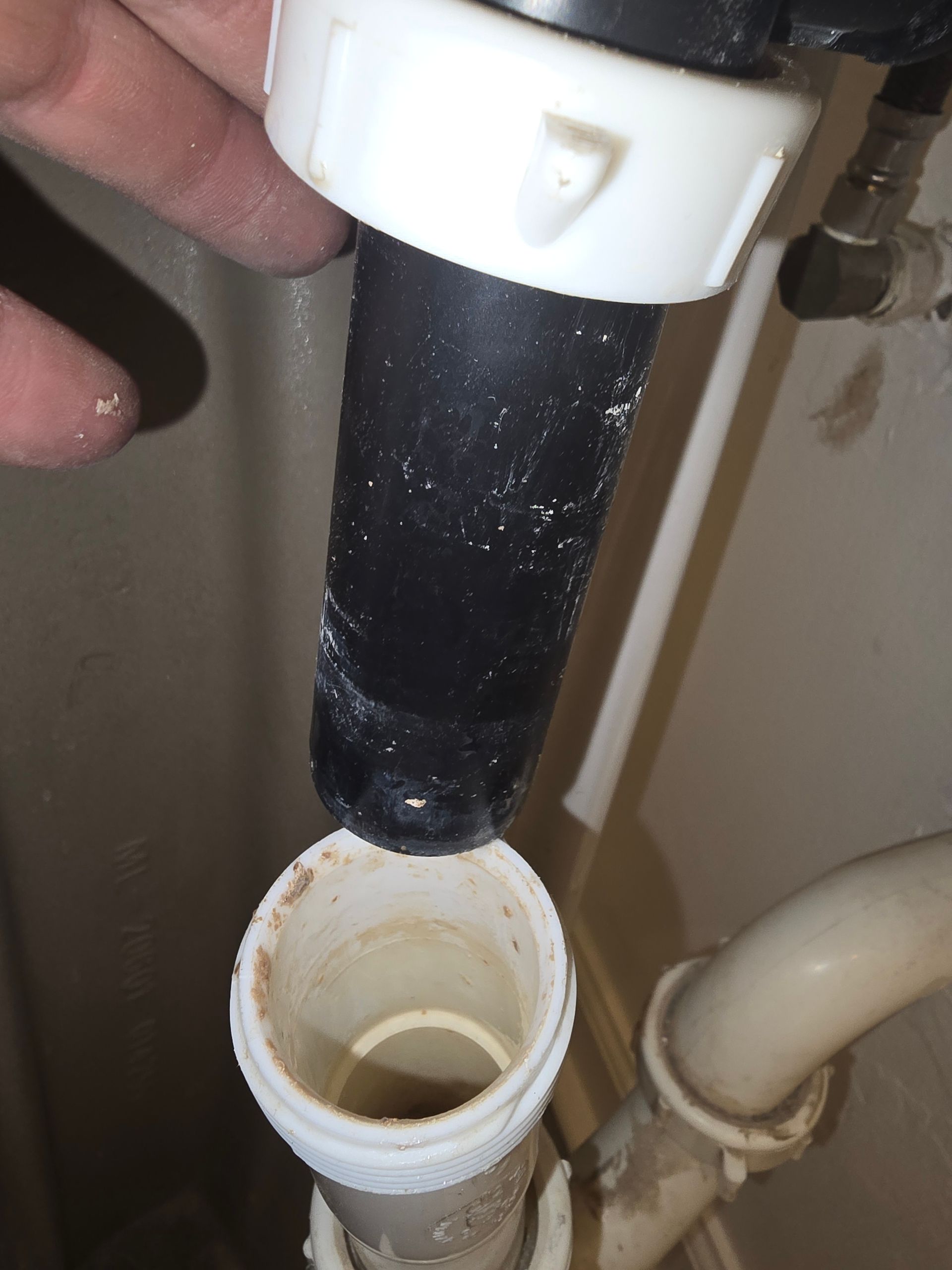 A black plastic sink pipe is disconnected and hovering above an open white drain pipe.