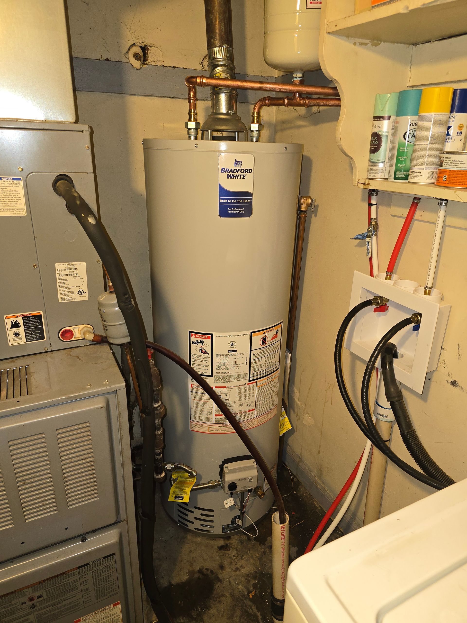 A grey residential water heater located in a small utility closet next to a furnace and laundry hookups.
