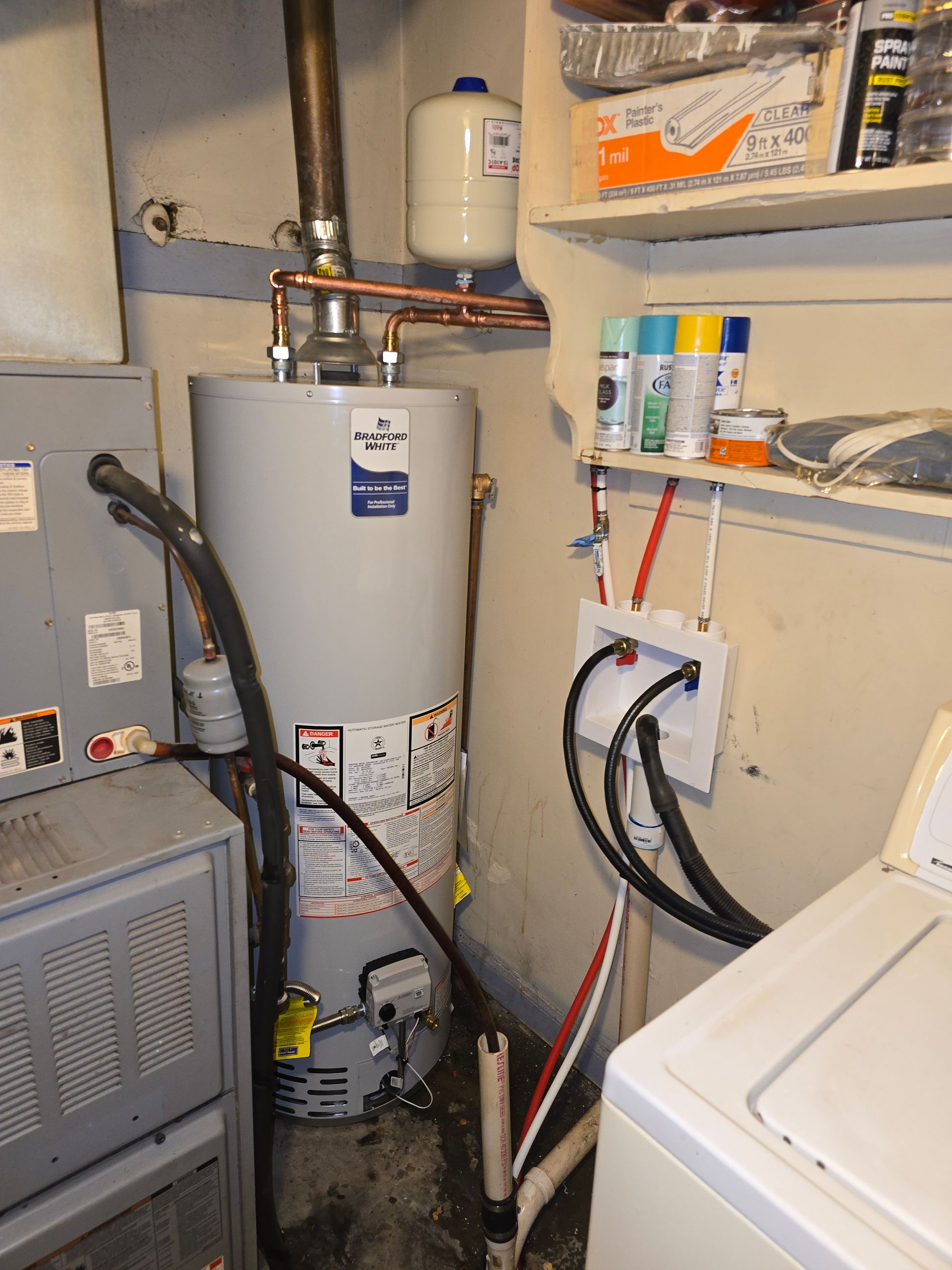 A water heater and HVAC unit in a utility room with a laundry setup and storage shelf nearby.