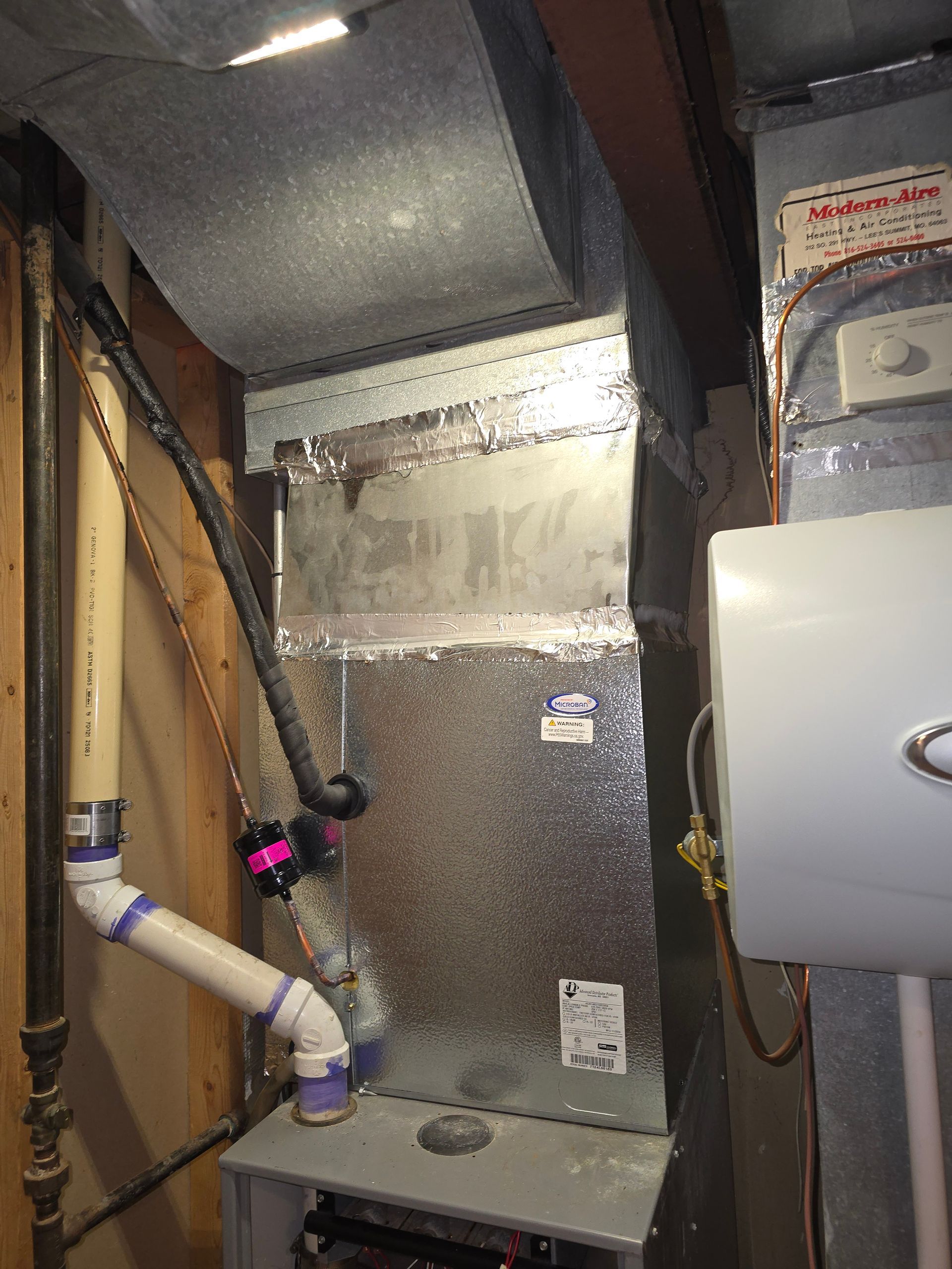 A metallic furnace unit with attached PVC exhaust pipes, installed in a utility space.