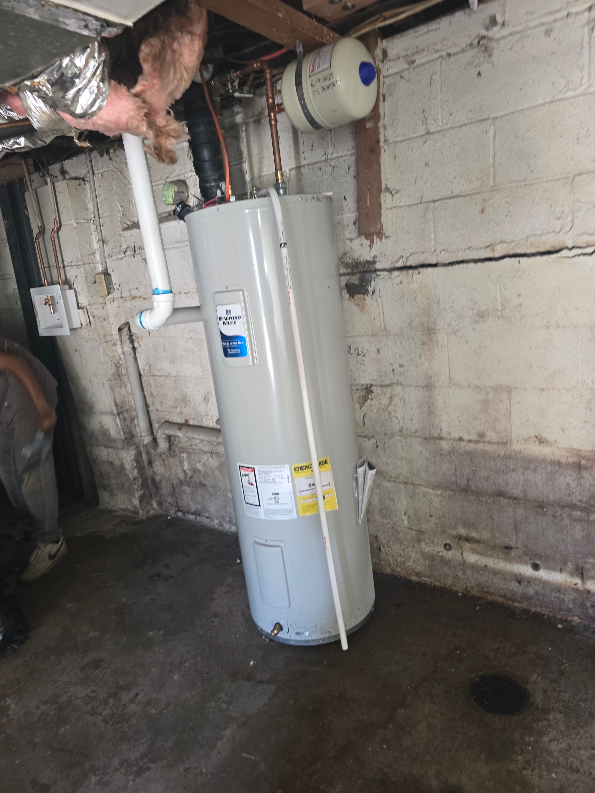 A gray residential water heater standing in a basement corner next to a concrete block wall.