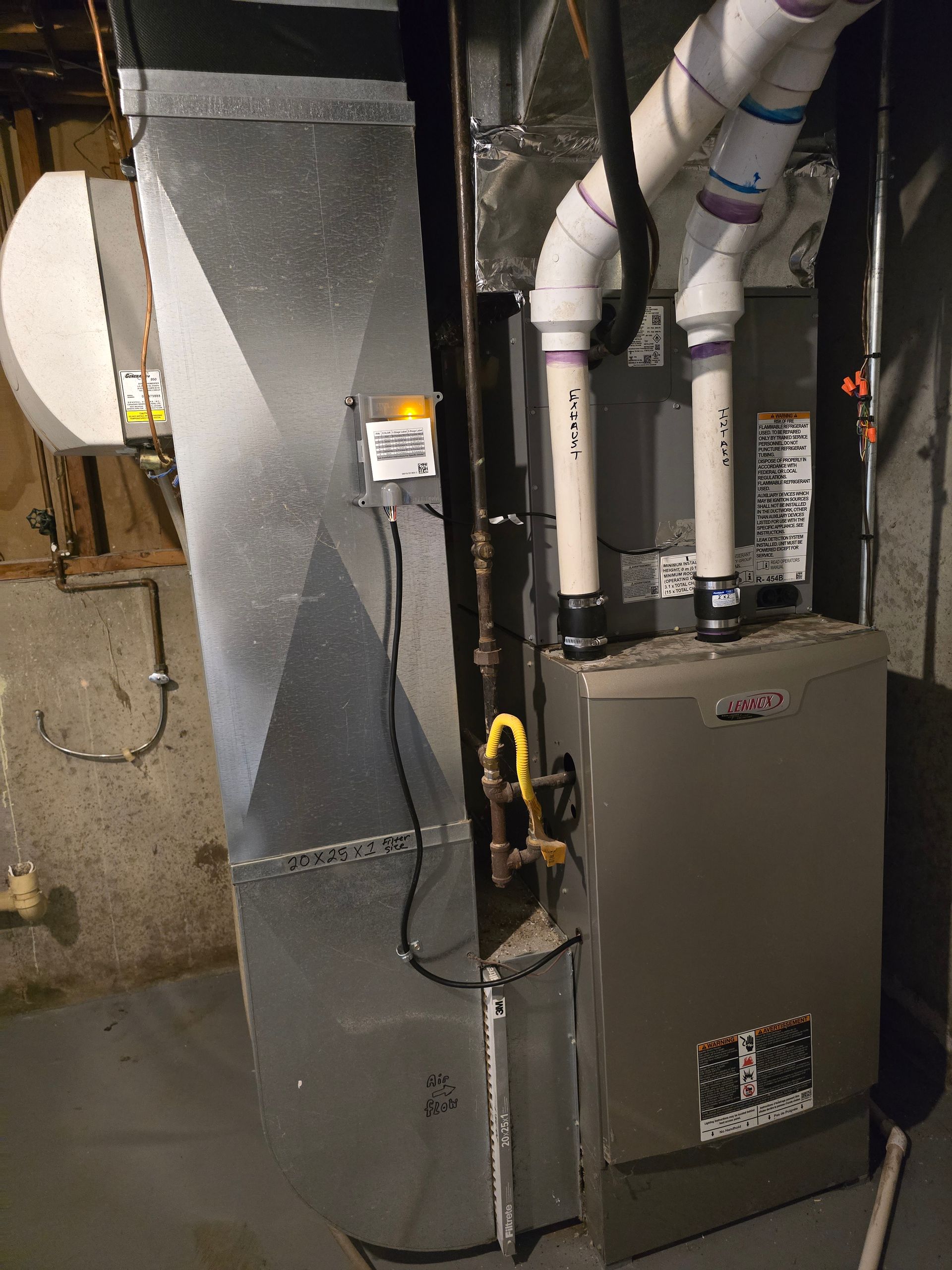 A vertical, high-efficiency gas furnace with white PVC venting pipes attached to a gray metal duct system in a basement.