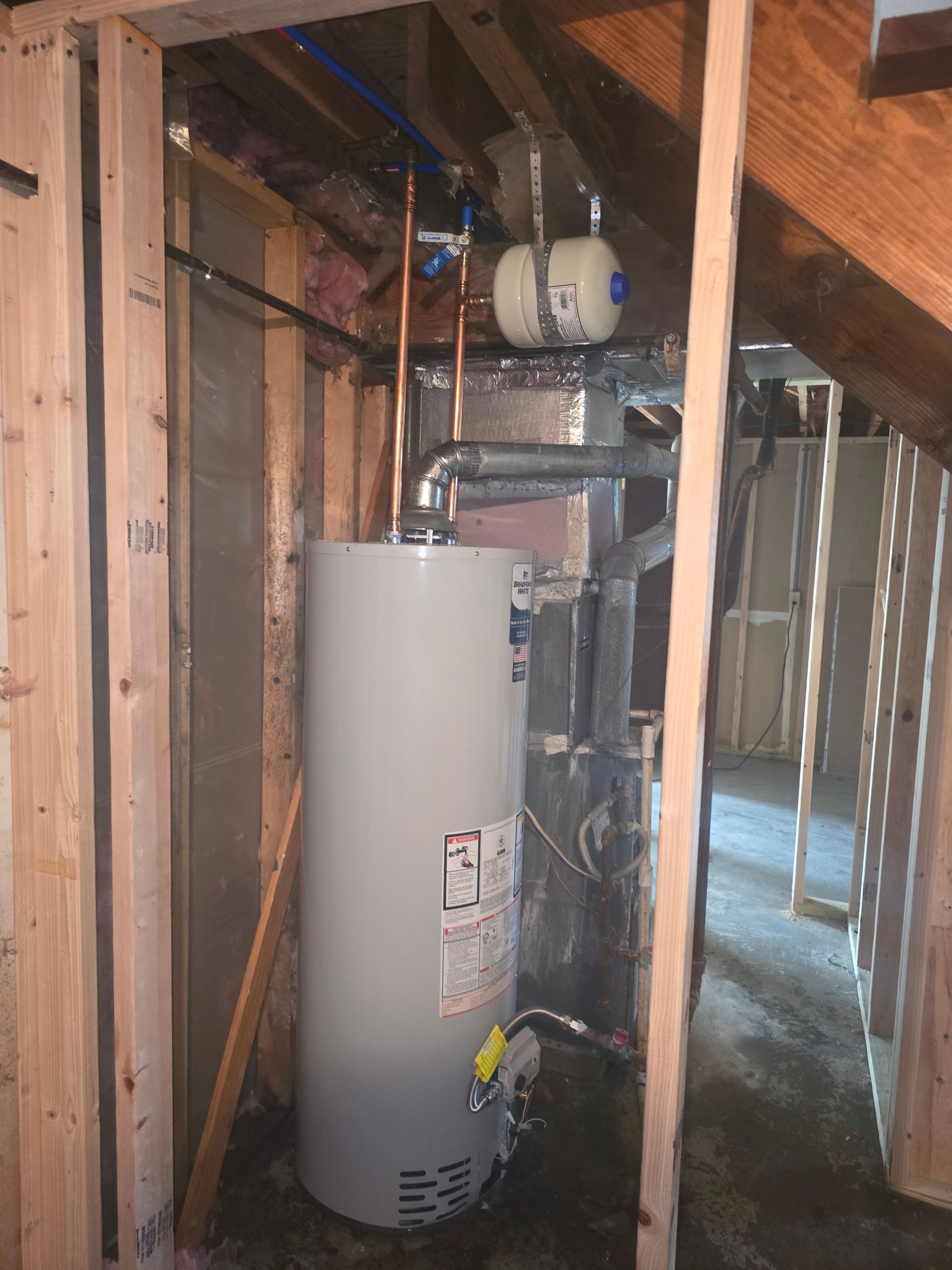 A residential water heater and an expansion tank installed in an unfinished basement area with wood framing.