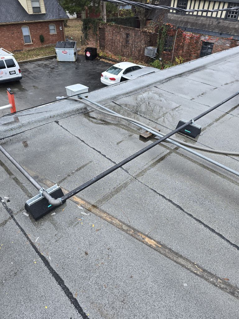 Conduit pipes mounted on black rubber roof blocks on a flat, gray commercial roof.