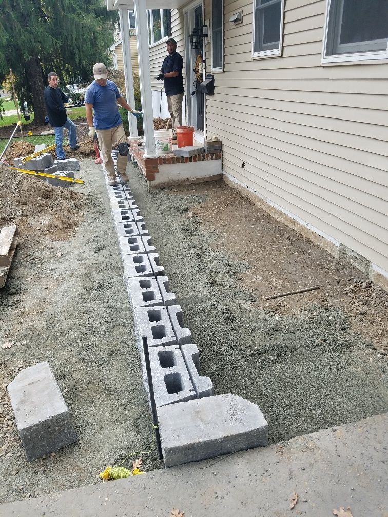 A group of men are working on a sidewalk in front of a house.