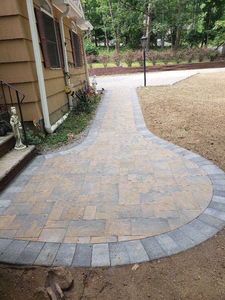 A brick walkway leading to a house next to a driveway.