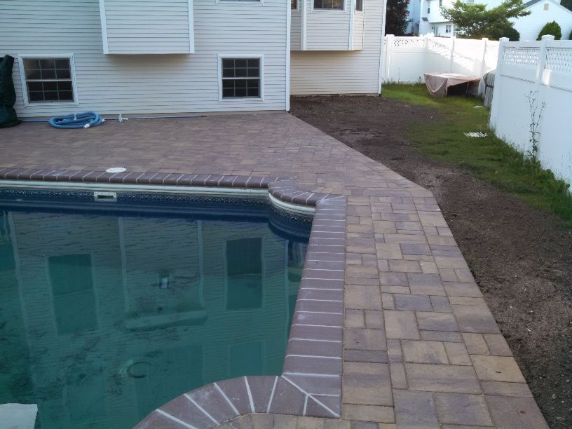 A large swimming pool surrounded by lawn chairs and umbrellas in a backyard.