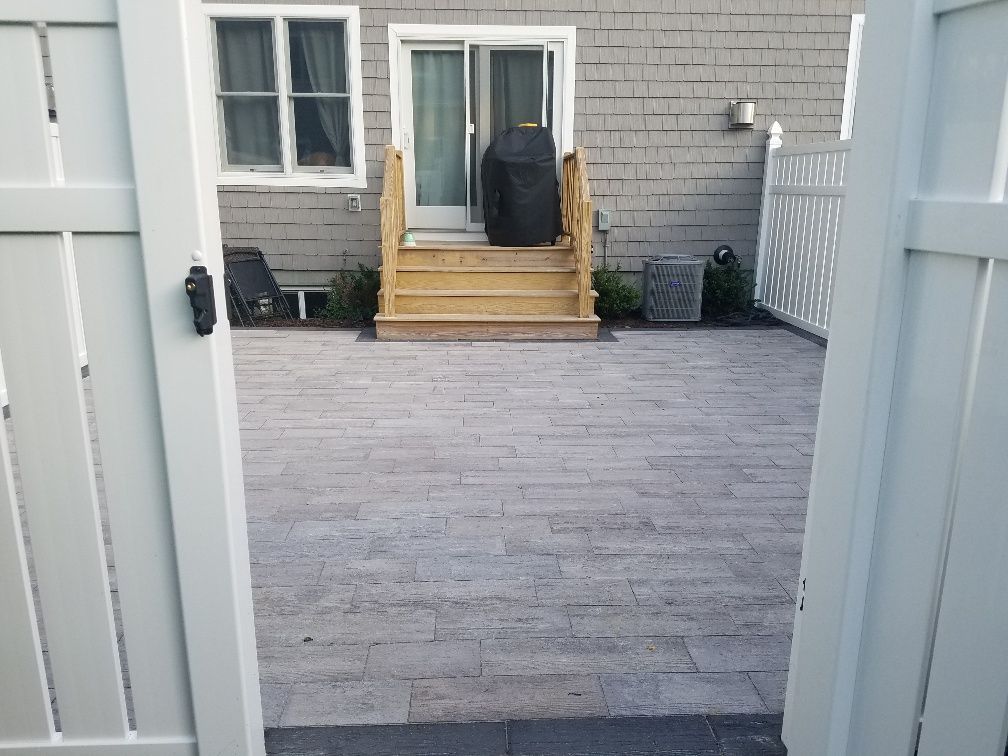 A white fence is open to a backyard with a grill and stairs.