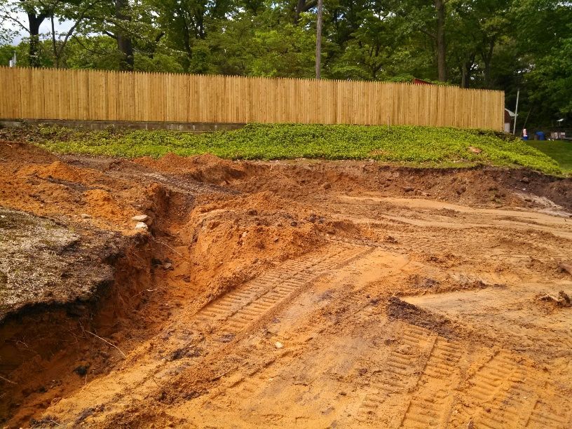 An excavator is digging a hole in the ground in front of a house.