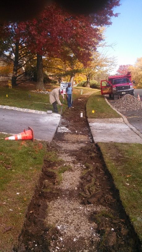 A group of people are working on a sidewalk next to a road.