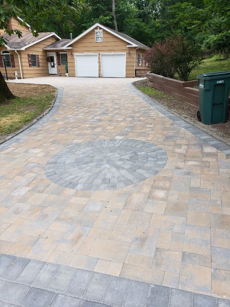 A driveway with a circular design in the middle is leading to a house.