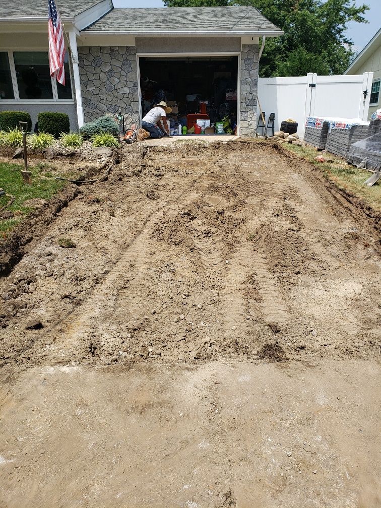 A man is working on a dirt driveway in front of a house.